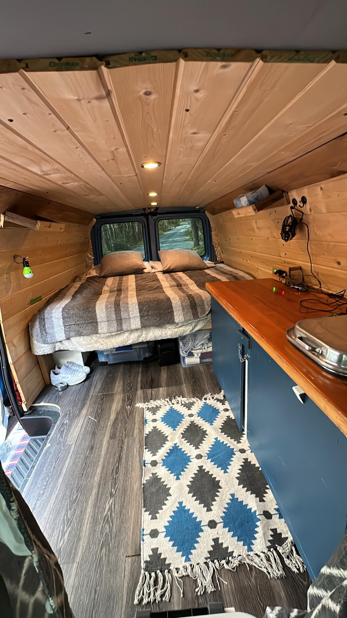 Cozy RV rental interior: wood-paneled ceiling, comfy bed, and full counter setup. Ready for your van life adventure.. Ford Econolline 250 2005