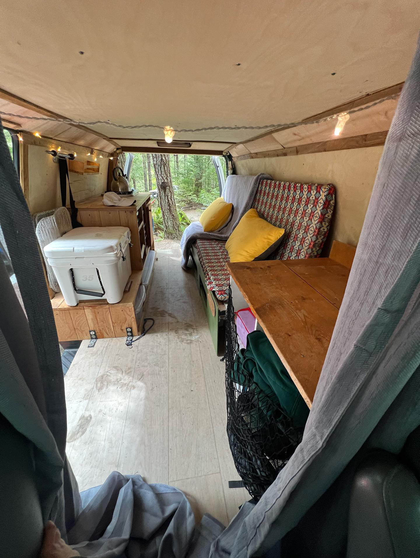 Experience van life! This RV rental features a cozy interior with a bed, kitchen, cooler, and forest view.. Ford Econoline 150 2007