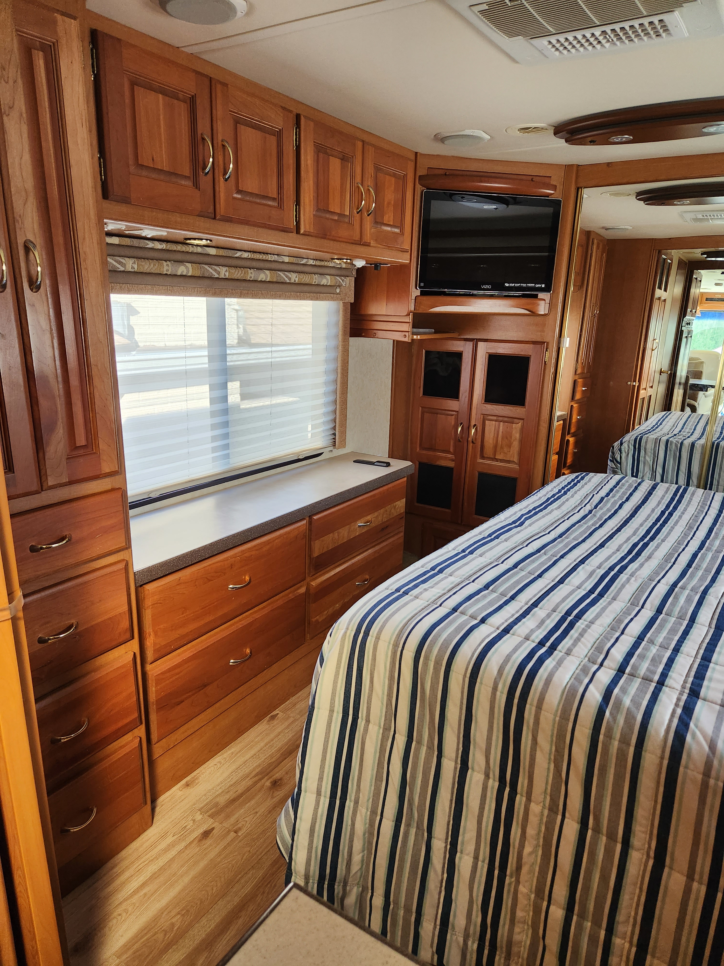 Inside an RV rental: cozy bedroom featuring two beds with striped comforters, warm wood cabinets, TV, and window.. Holiday Rambler Endeavor 2003
