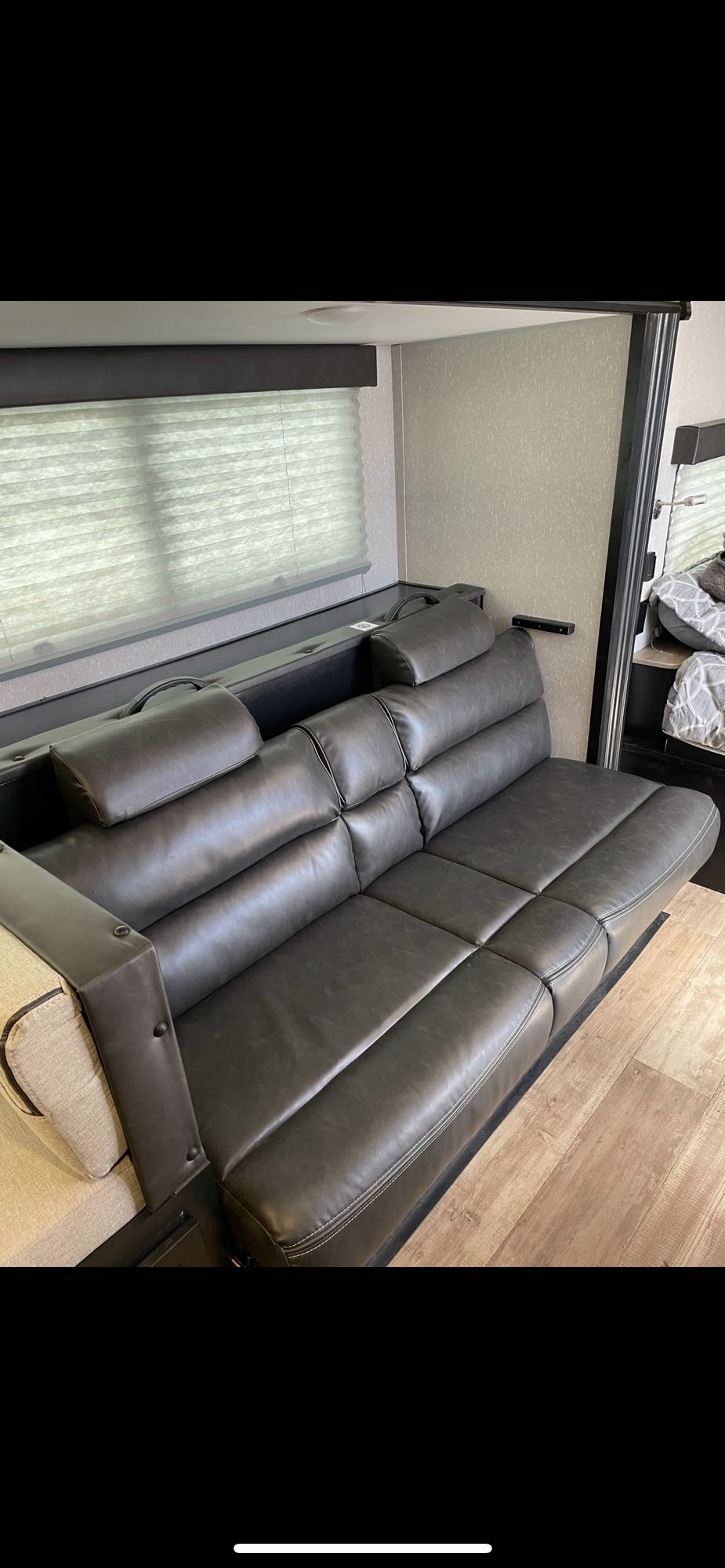 Dark gray leather convertible sofa inside a modern RV rental, featuring window blinds and wood flooring.. Forest River Cherokee Wolf Pup Black Label 2022