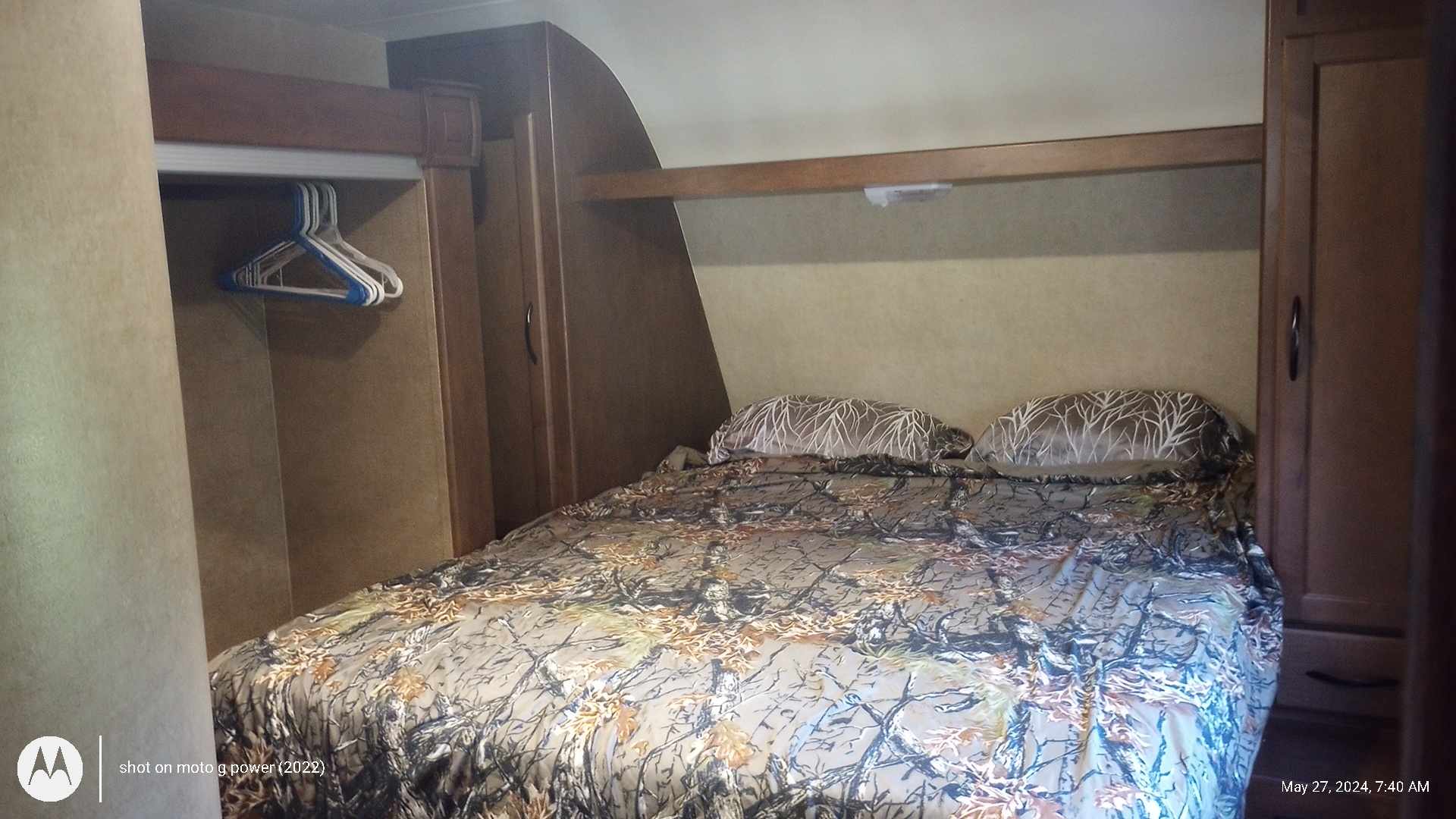 Compact RV rental bedroom featuring a bed with camouflage bedding, integrated wooden cabinetry, and a small hanging closet.. Pacific Coachworks Northland 2016