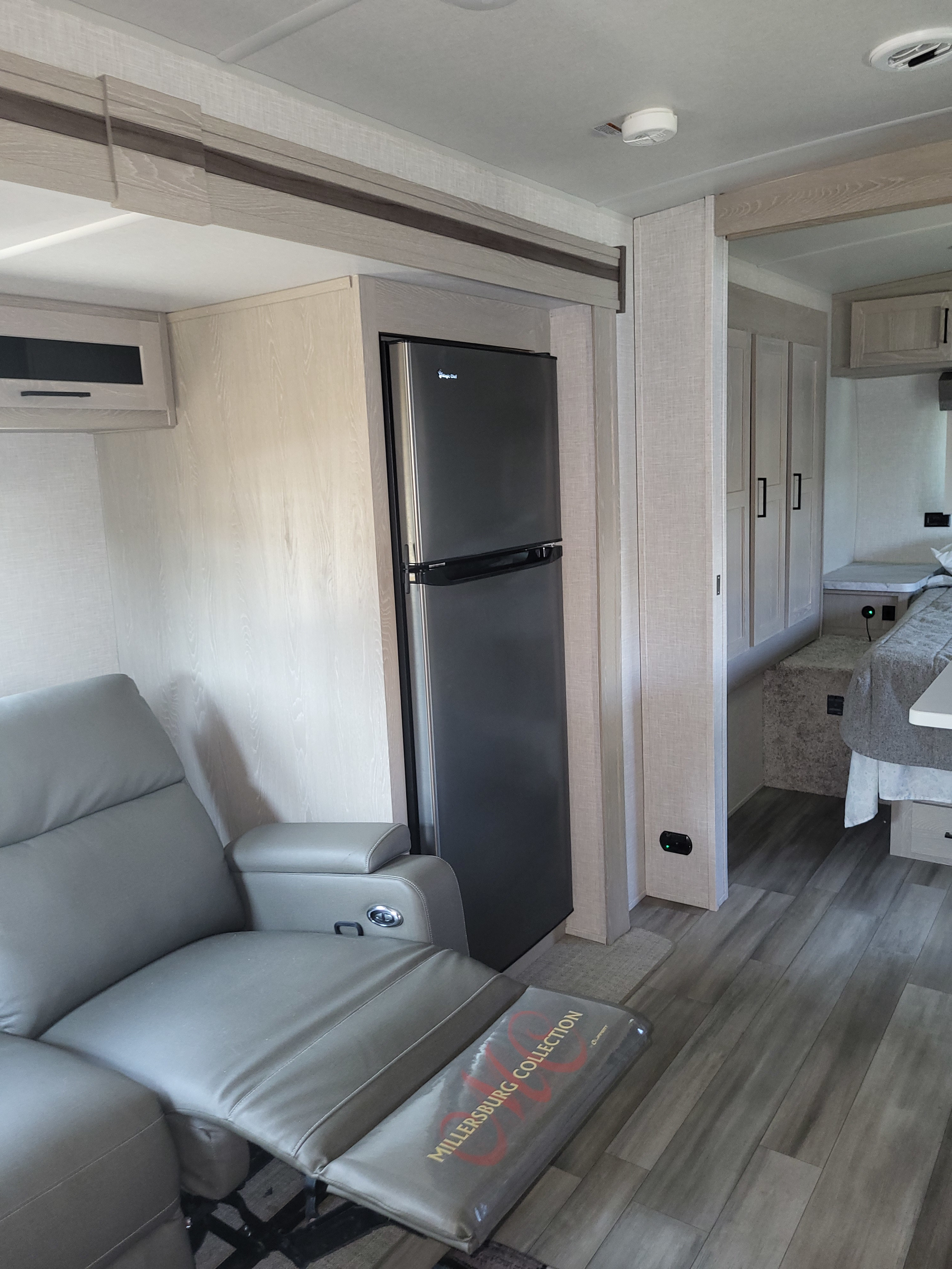 Step inside this RV rental: a modern interior featuring a gray recliner, full-size fridge, and open access to the bedroom.. Forest River Flagstaff Micro Lite 2023