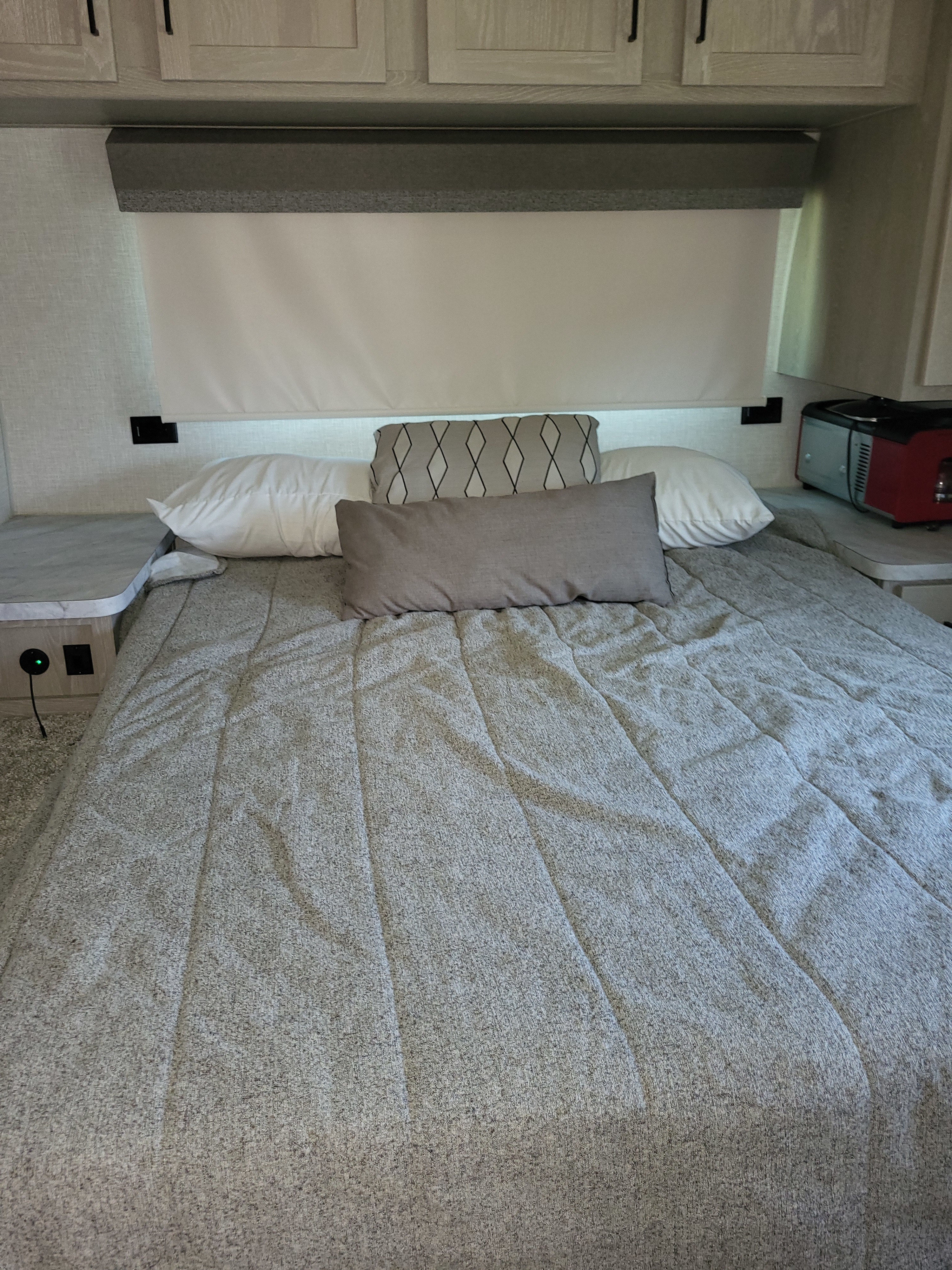 Cozy RV rental bedroom featuring a neatly made bed with grey bedding, white pillows, overhead cabinets, and side counters.. Forest River Flagstaff Micro Lite 2023