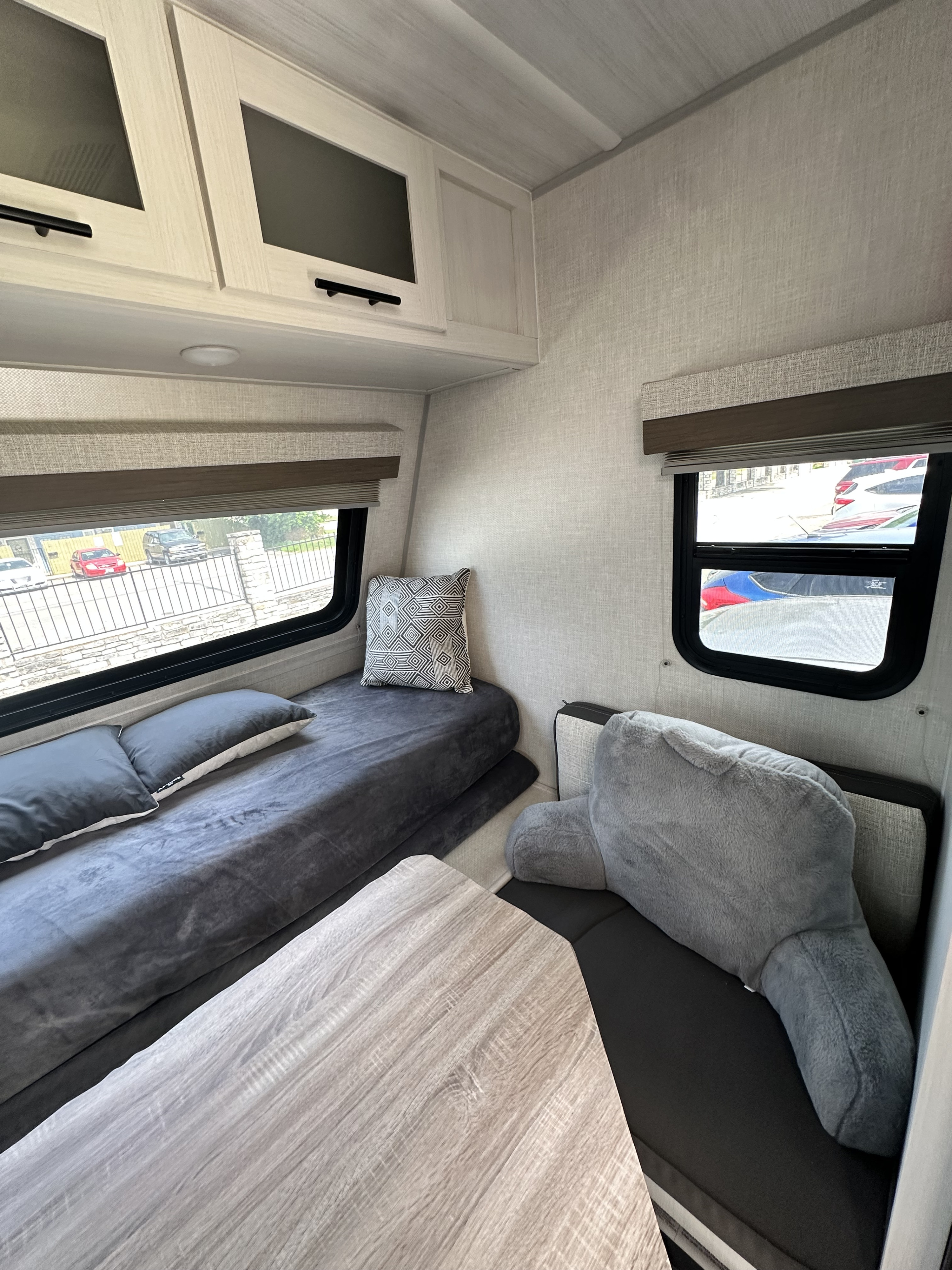 Cozy RV rental interior featuring a compact dinette with a light wood table, a bed/seating area, and overhead cabinets.. Forest River No Boundaries 16.1 2023