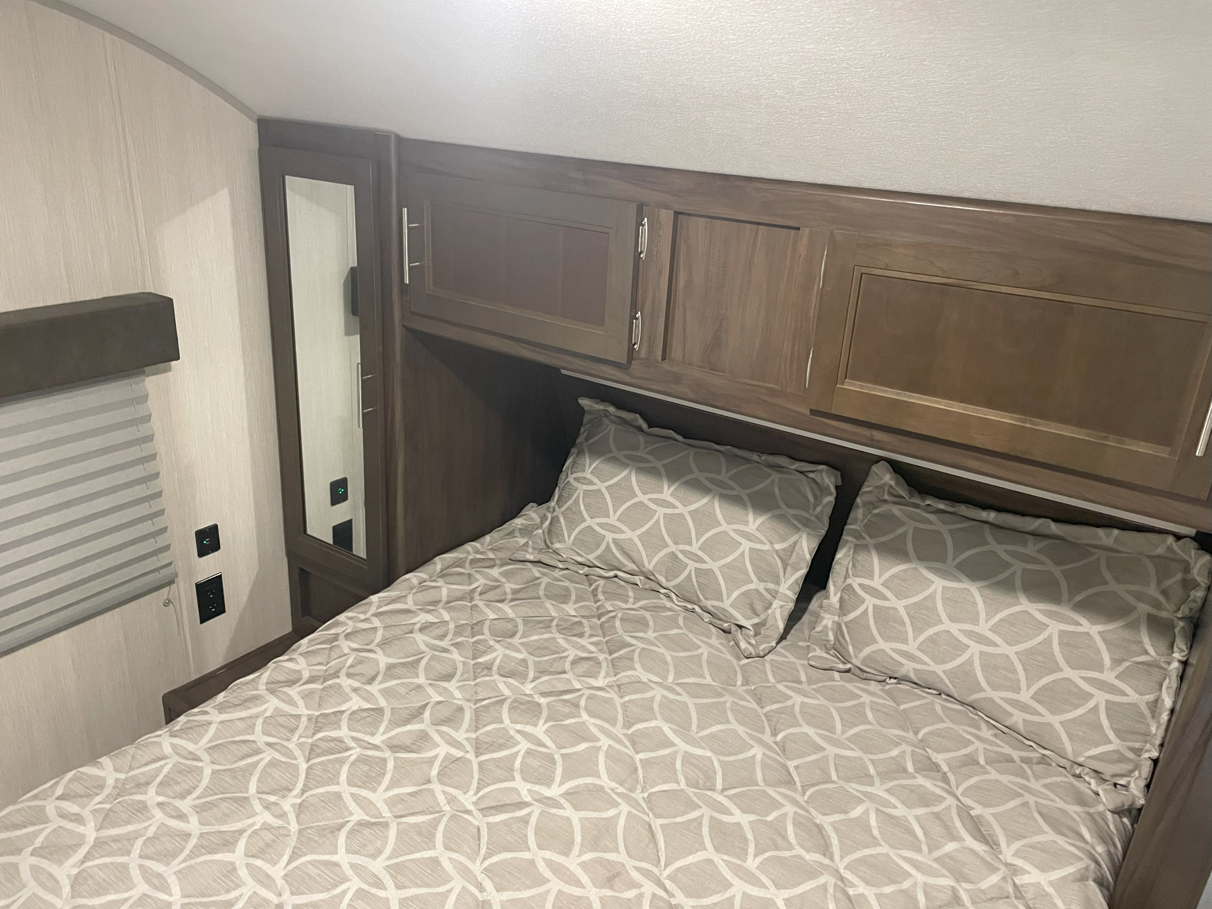 RV rental bedroom with patterned bedding, overhead storage, outlets & mirror. Compact comfort for travel.. Forest River Cherokee Grey Wolf 2019