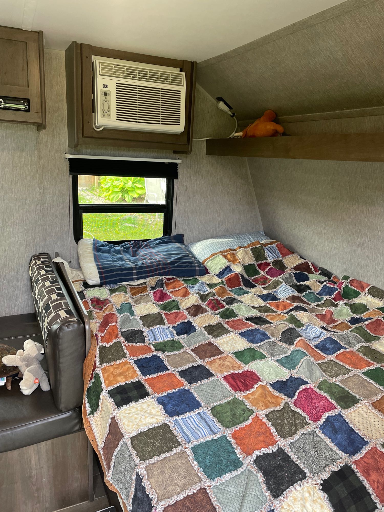 RV rental: cozy interior with a colorful rag quilt on the bed, sofa, window view, and AC unit.. Coleman 17FQ 2019