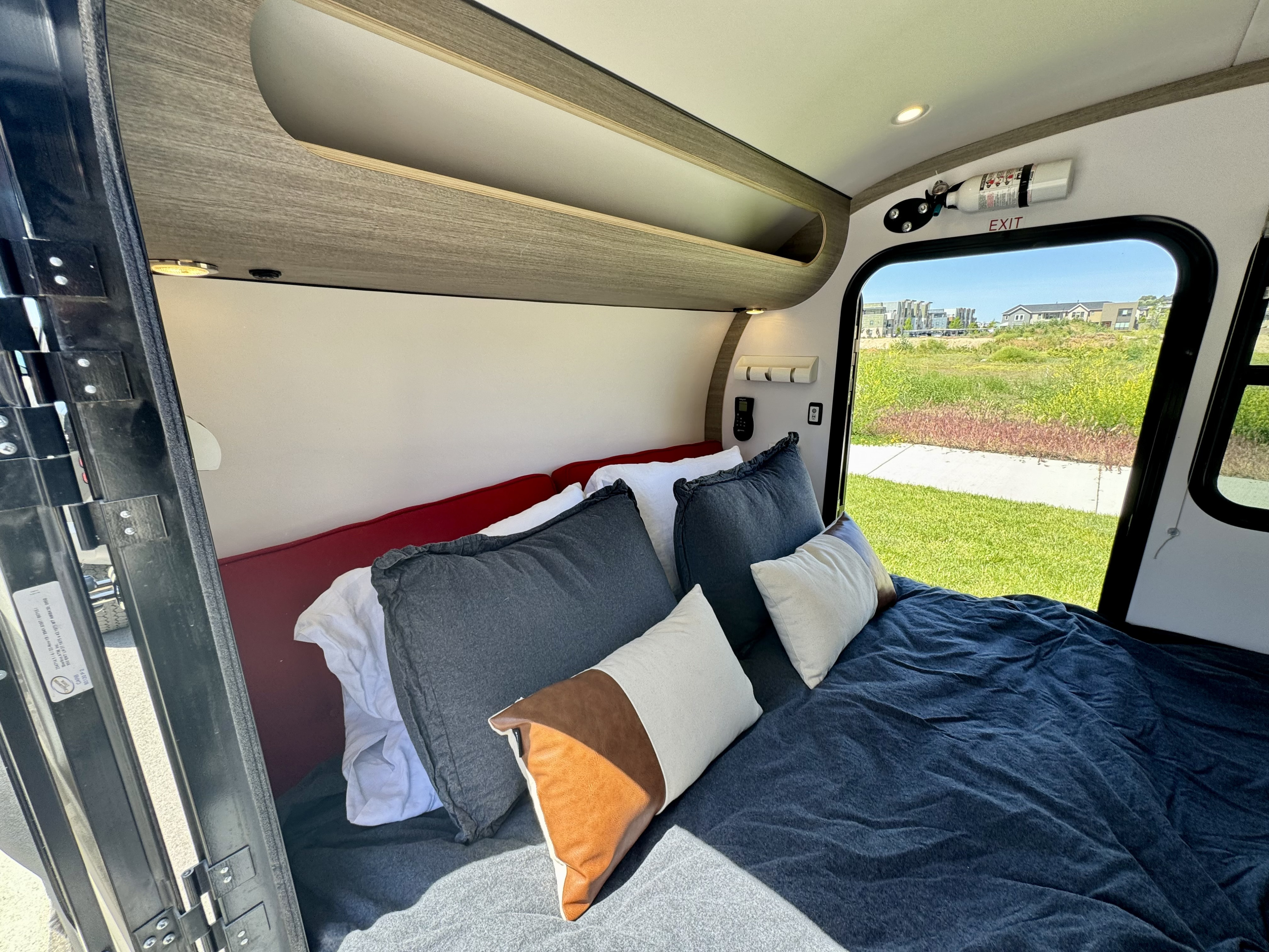 RV rental interior: A cozy bedroom with a bed, overhead storage, a fire extinguisher, and a scenic window view.. Bean Trailer Bean Trailer Trailer 2019