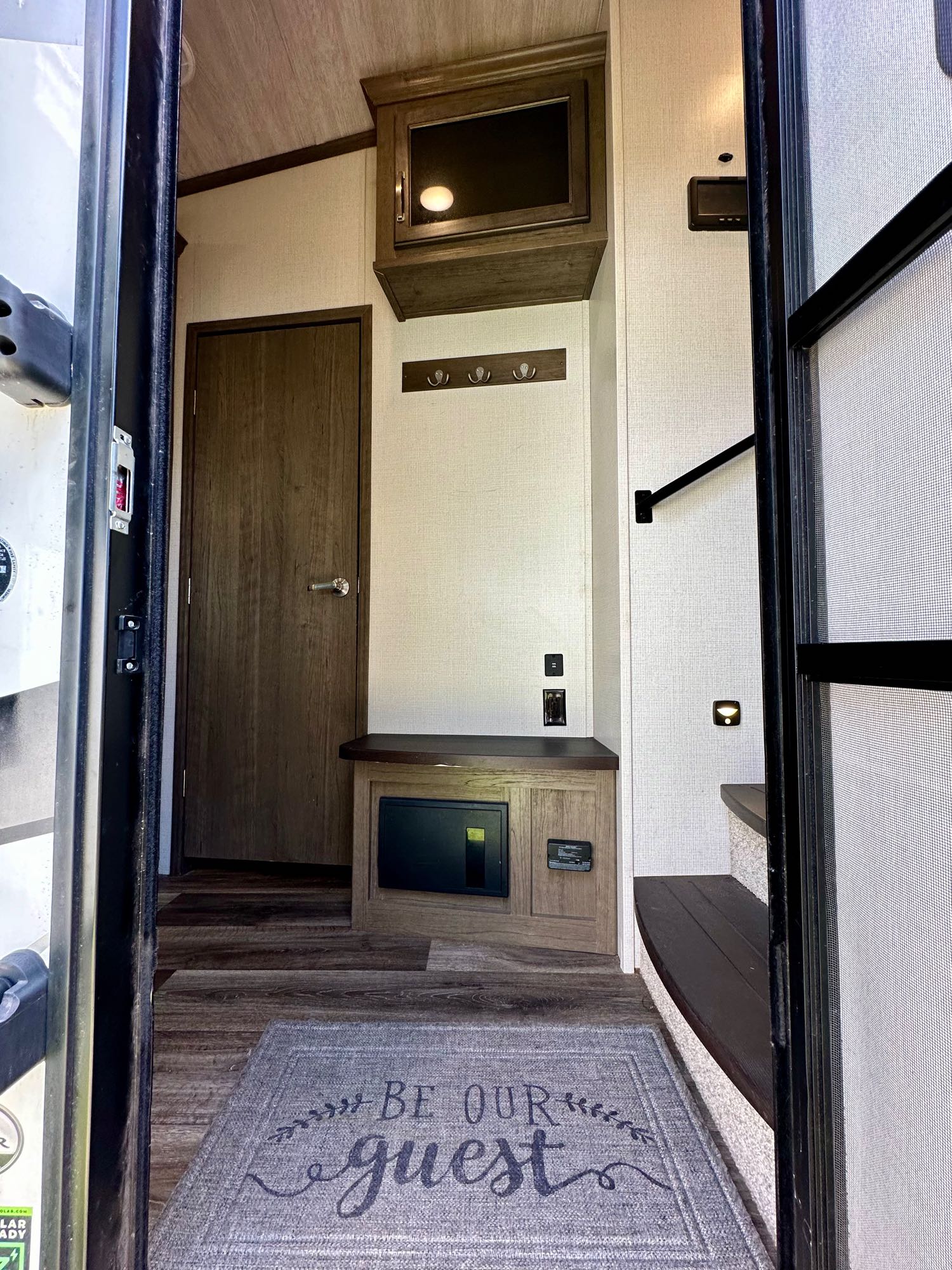 RV rental interior: A welcoming entryway with a "Be Our Guest" mat, built-in storage, a door, and stairs.. Keystone RV Cougar 2021