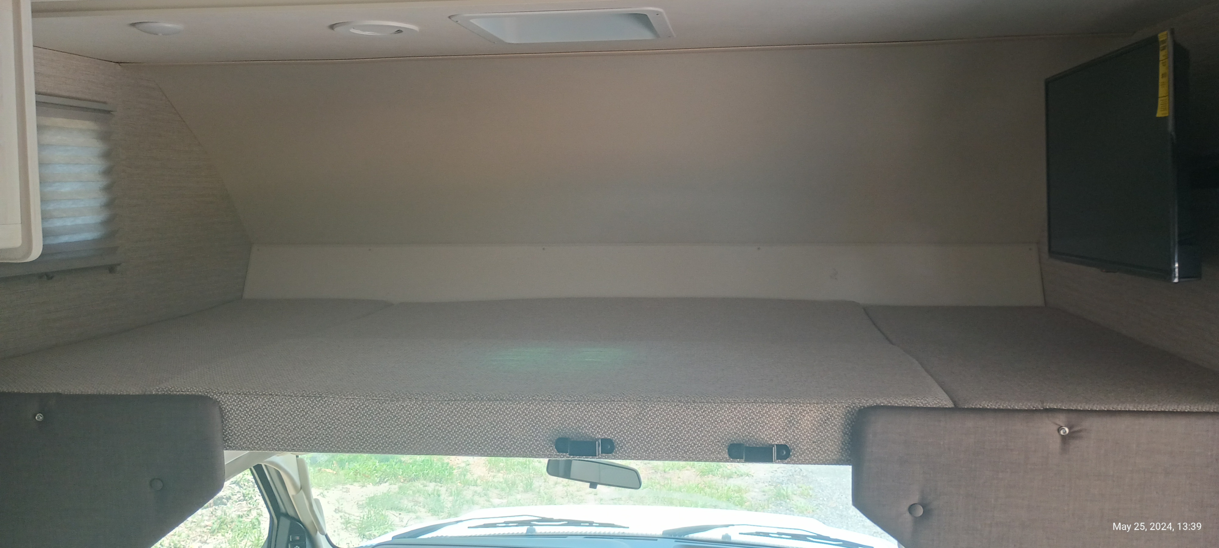 Spacious cab-over bunk bed with TV and window inside an RV rental. Ideal for a comfortable sleep space.. Winnebago Outlook 2021