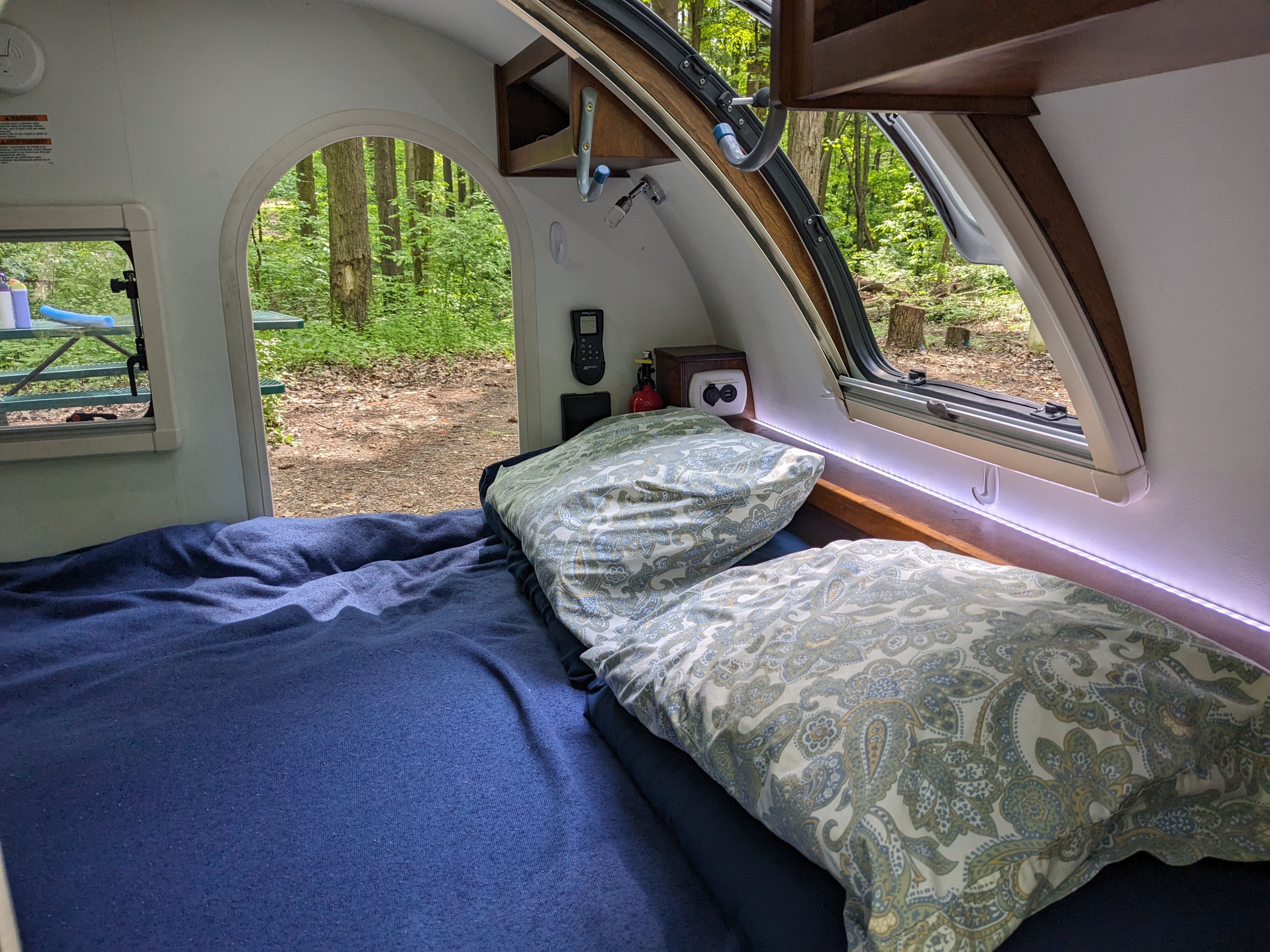 Inside a cozy RV rental camper with a bed, facing an archway view of a serene forest. Ideal for nature retreats.. nuCamp T@G 2018