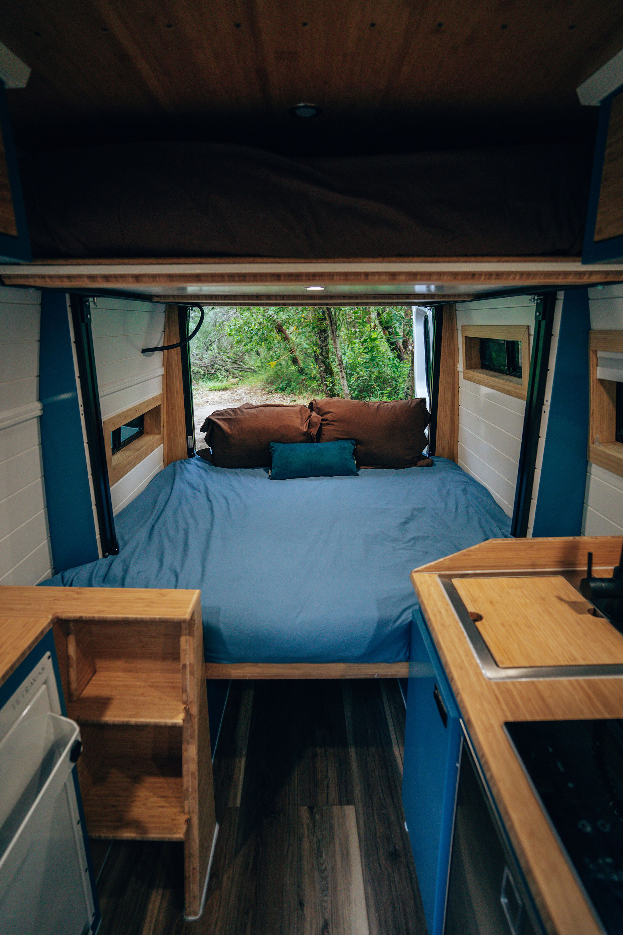 Inside a cozy **rv rental**: comfy bed, kitchen area, and nature views through open back doors.. Mercedes-Benz Sprinter 2024