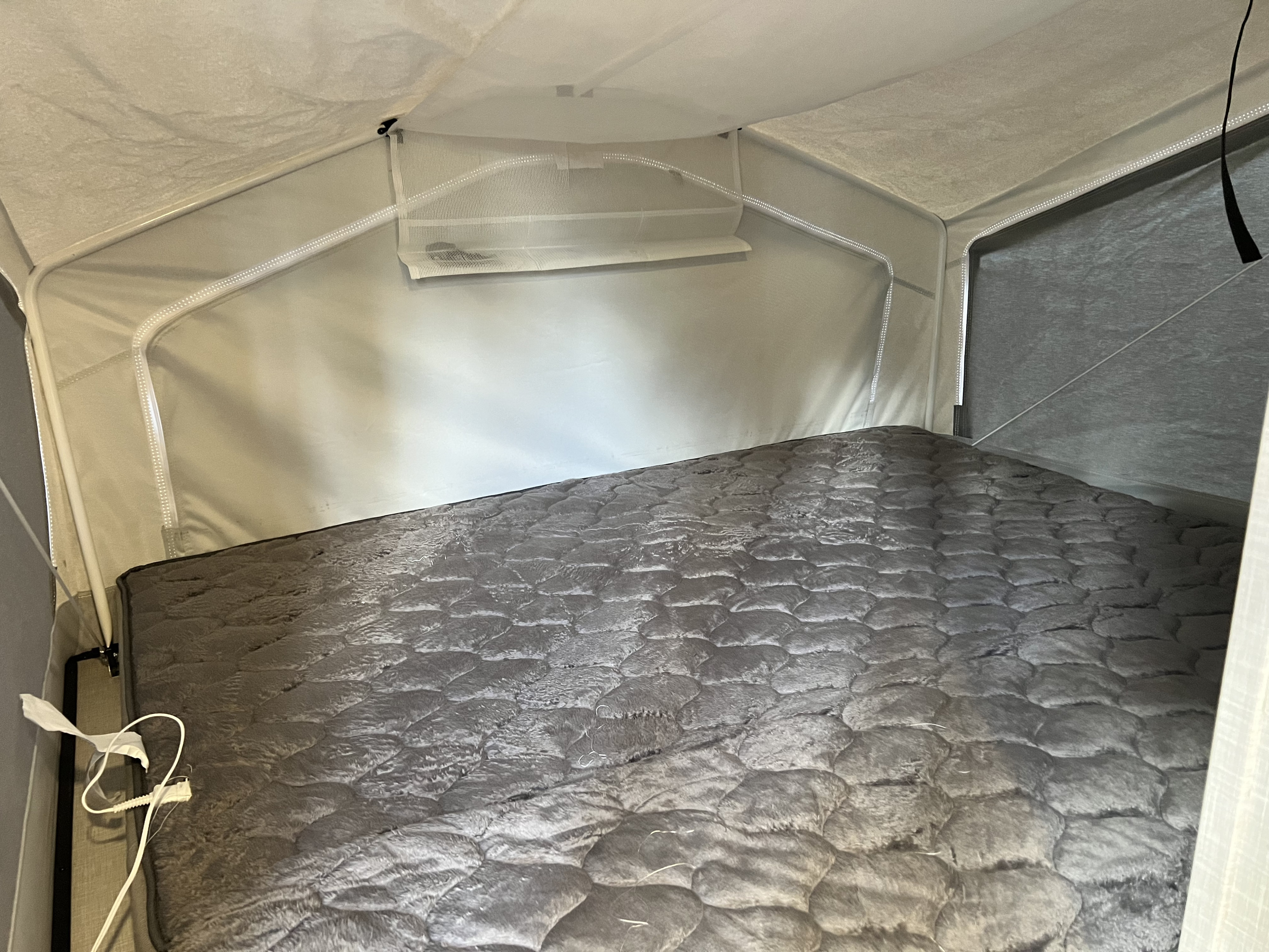 Pop-up RV rental bed with a soft grey quilted blanket and ambient strip lighting. Cozy camper interior ready for rest.. Forest River Rockwood Roo 2022