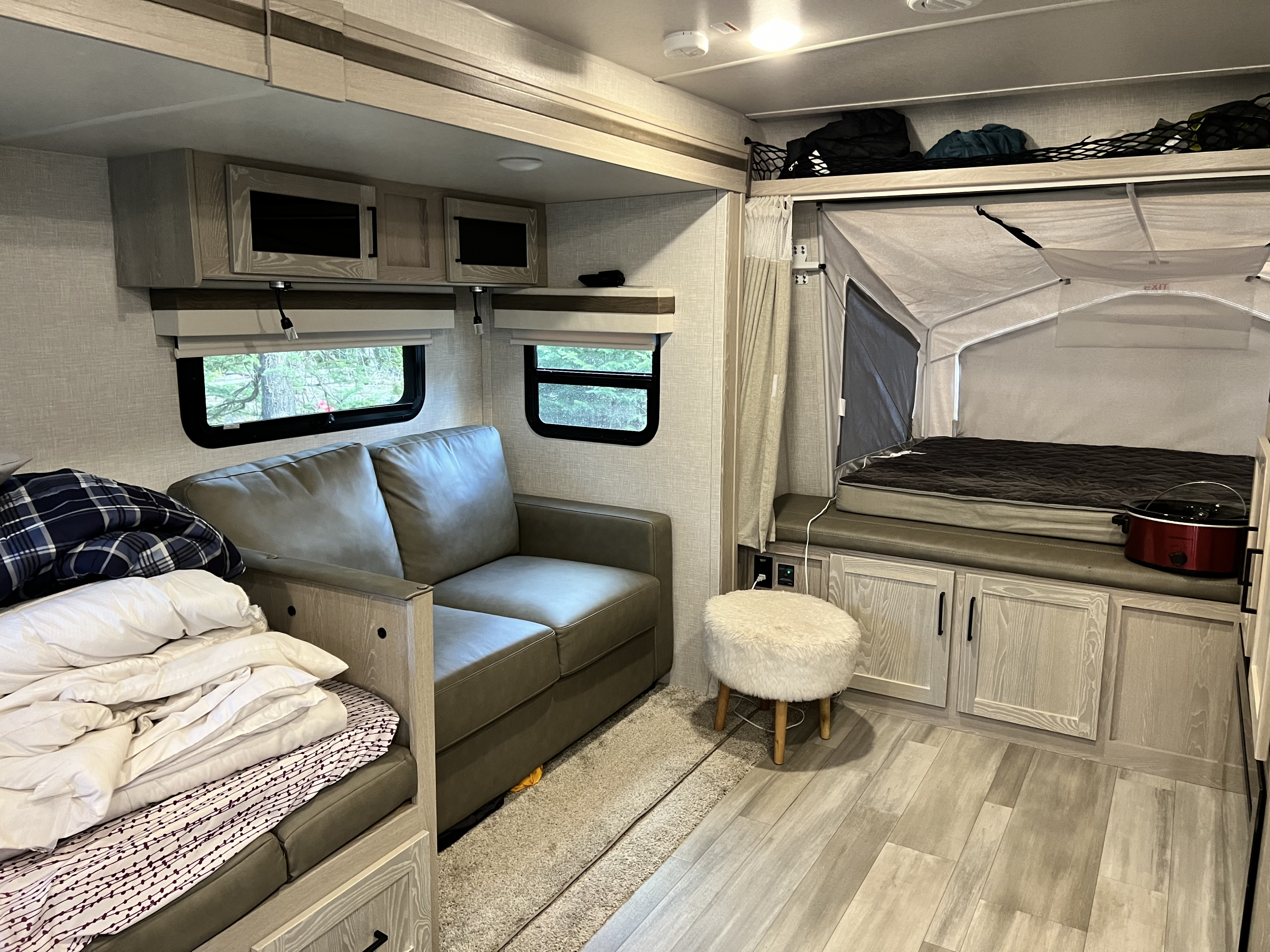 Inside a modern rv rental: a cozy living space with a sofa, pop-out bed, overhead cabinets, and windows for natural light.. Forest River Rockwood Roo 2022