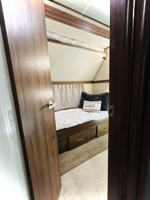 Cozy RV rental bedroom features a bed with under-bed storage, angled ceiling, and light walls framed by wood doors.. Palomino Columbus Castaway 2019
