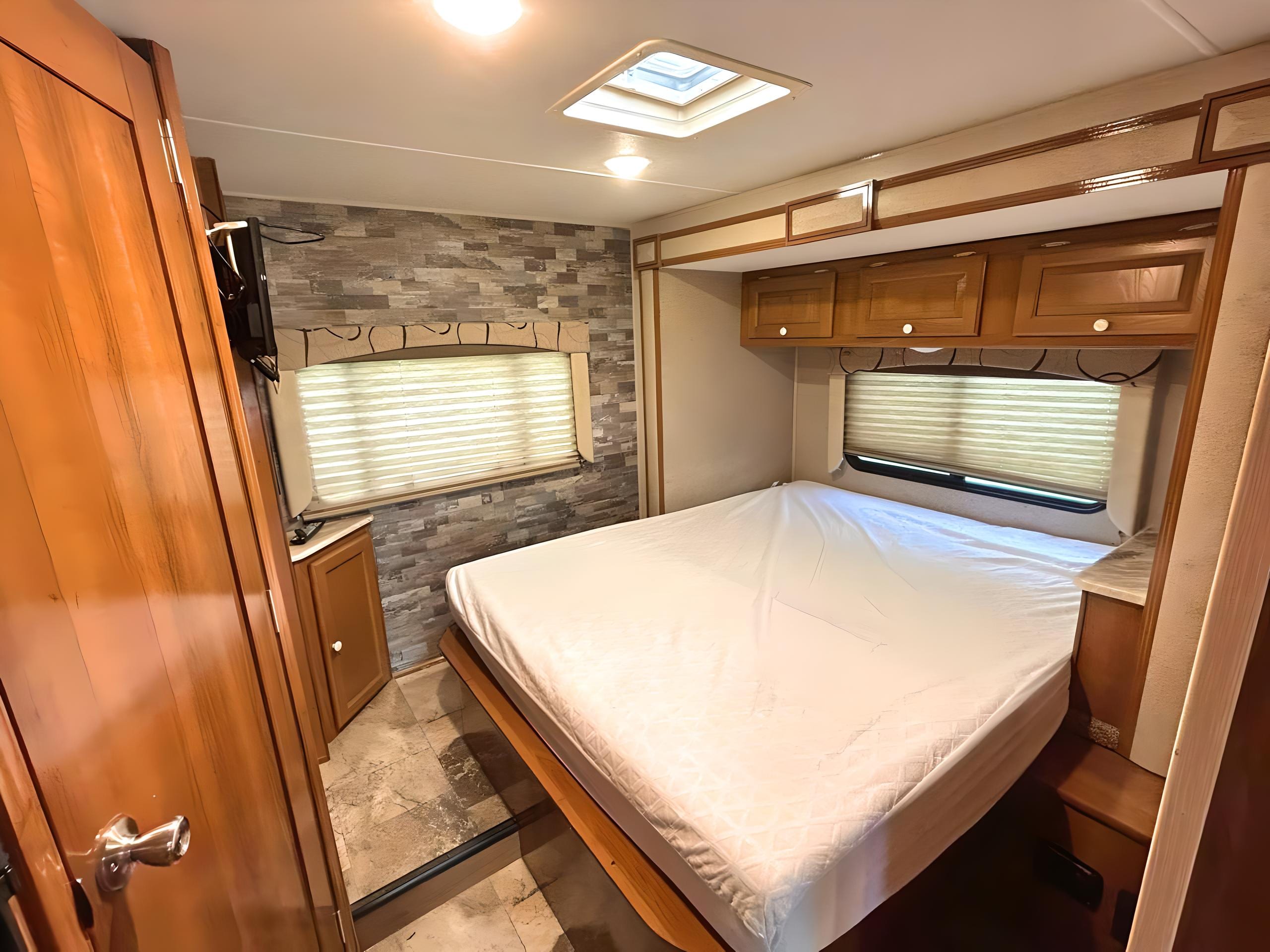 Cozy RV rental bedroom with a bed, overhead cabinets, TV, and skylight for bright travel.. COACHMEN LEPRECHAUN 2017