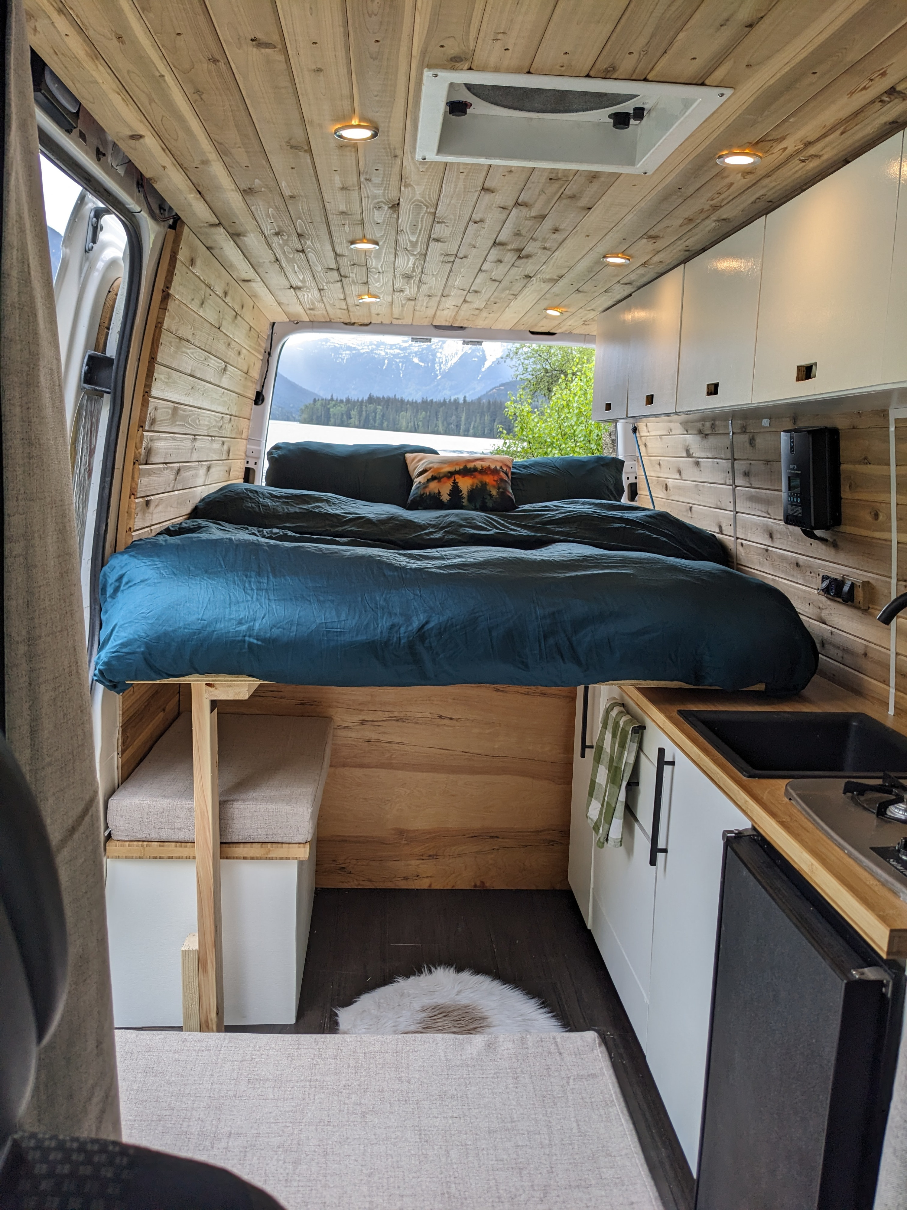 Cozy RV rental interior with a comfy bed, kitchenette, wood finish, and stunning mountain lake view. Perfect for adventures!. Dodge Sprinter Van 2007