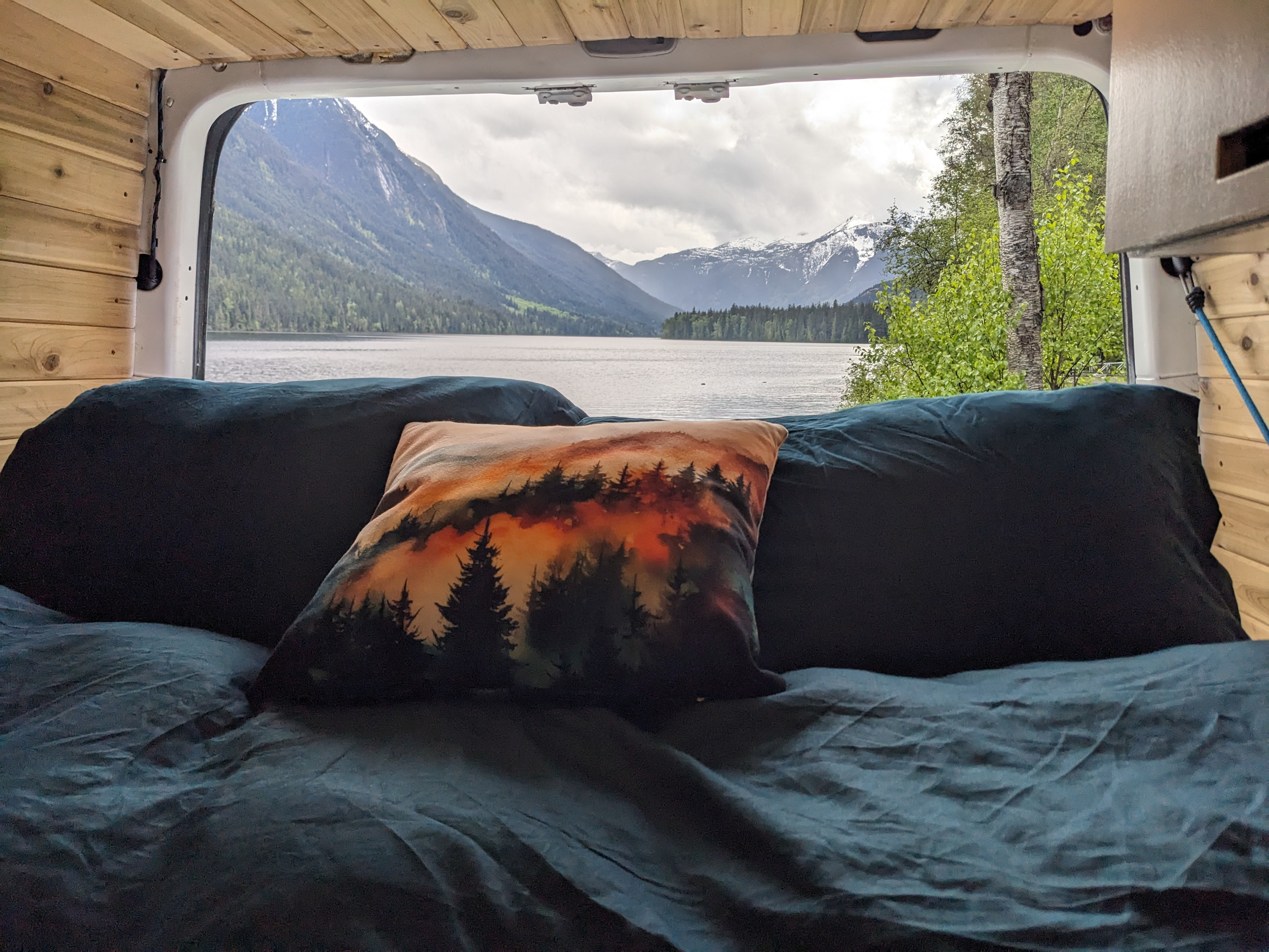 Inside a cozy RV rental: a comfortable bed with a scenic view of a vast mountain lake and snow-capped peaks.. Dodge Sprinter Van 2007