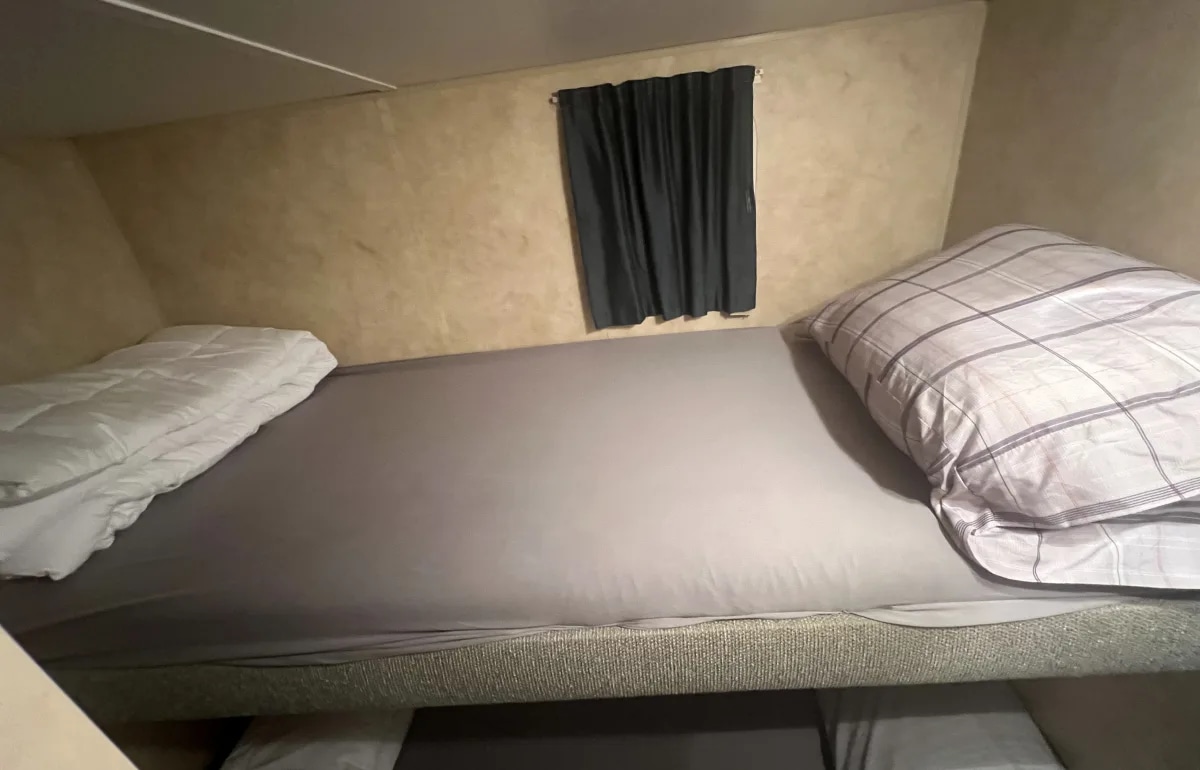 RV rental bunk bed view: a compact sleeping space with gray sheets, folded duvet, plaid comforter, and window.. Jayco Jay Flight 2006