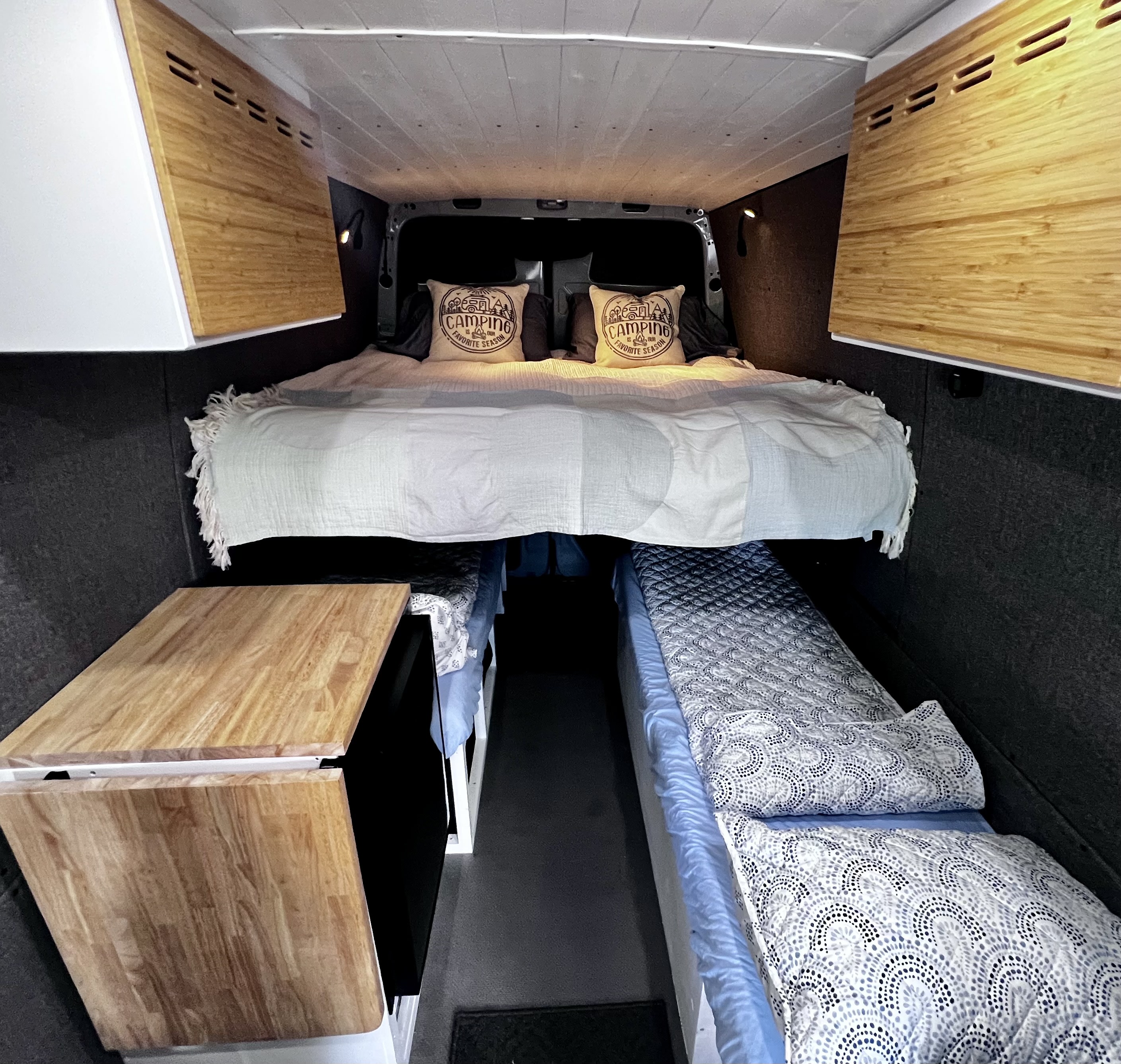 Cozy RV rental interior showing a raised bed, patterned lower bunk, and wood countertop, perfect for van life.. Mercedes-Benz Sprinter 2022
