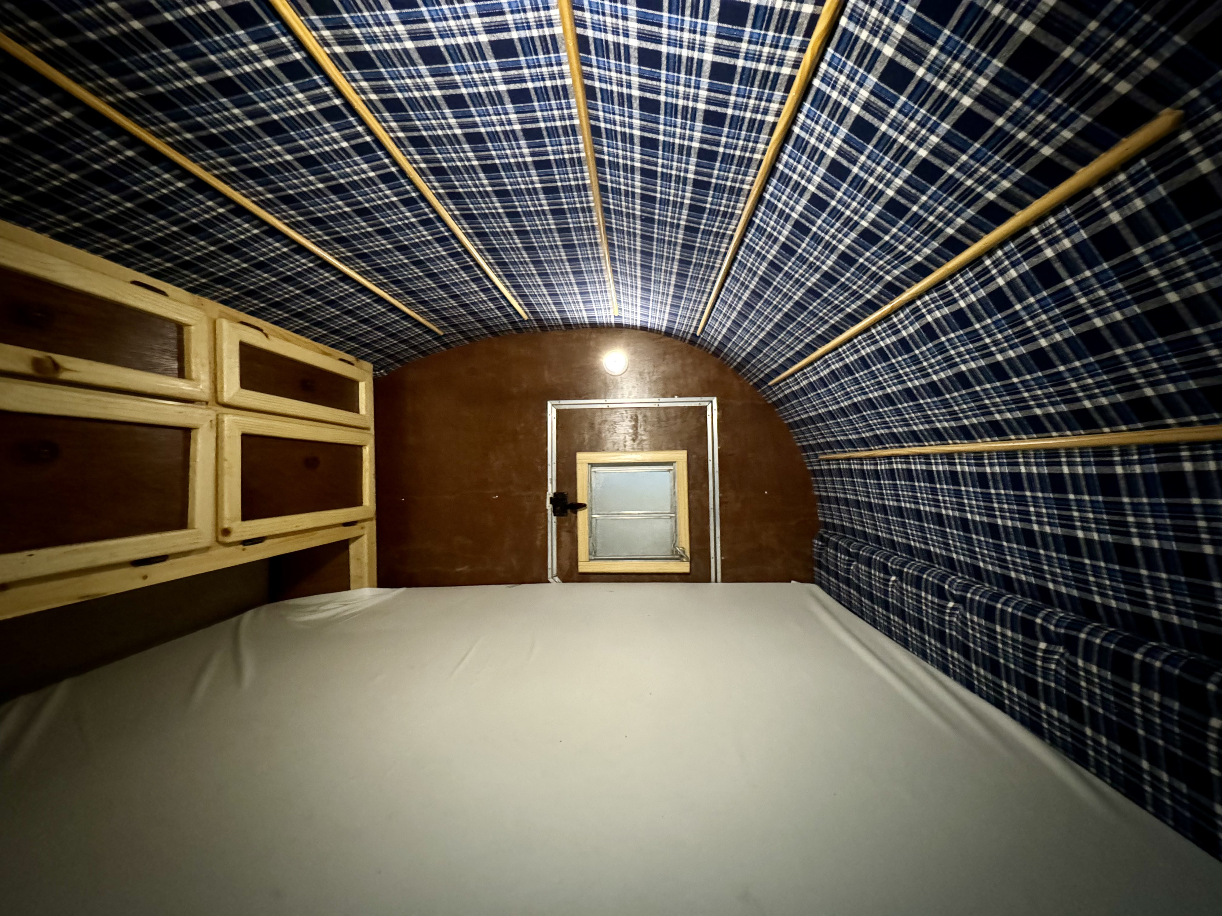 RV rental's cozy interior features a comfy bed, wood storage, and distinctive blue plaid ceiling.. Custom Build n/a 2015