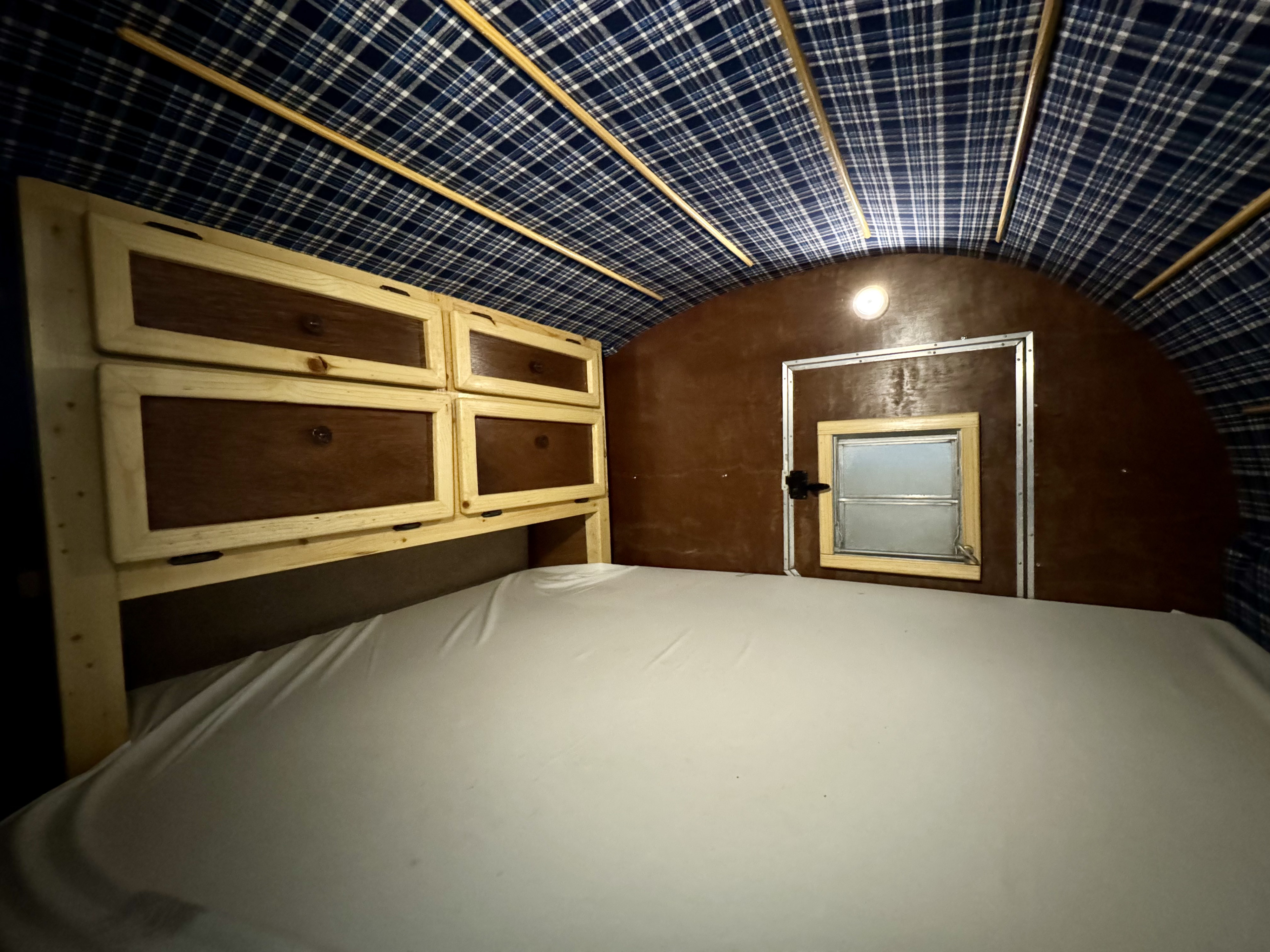 This cozy RV rental interior features a bed, wooden cabinets, and a blue plaid ceiling. Ideal for travel adventures.. Custom Build n/a 2015