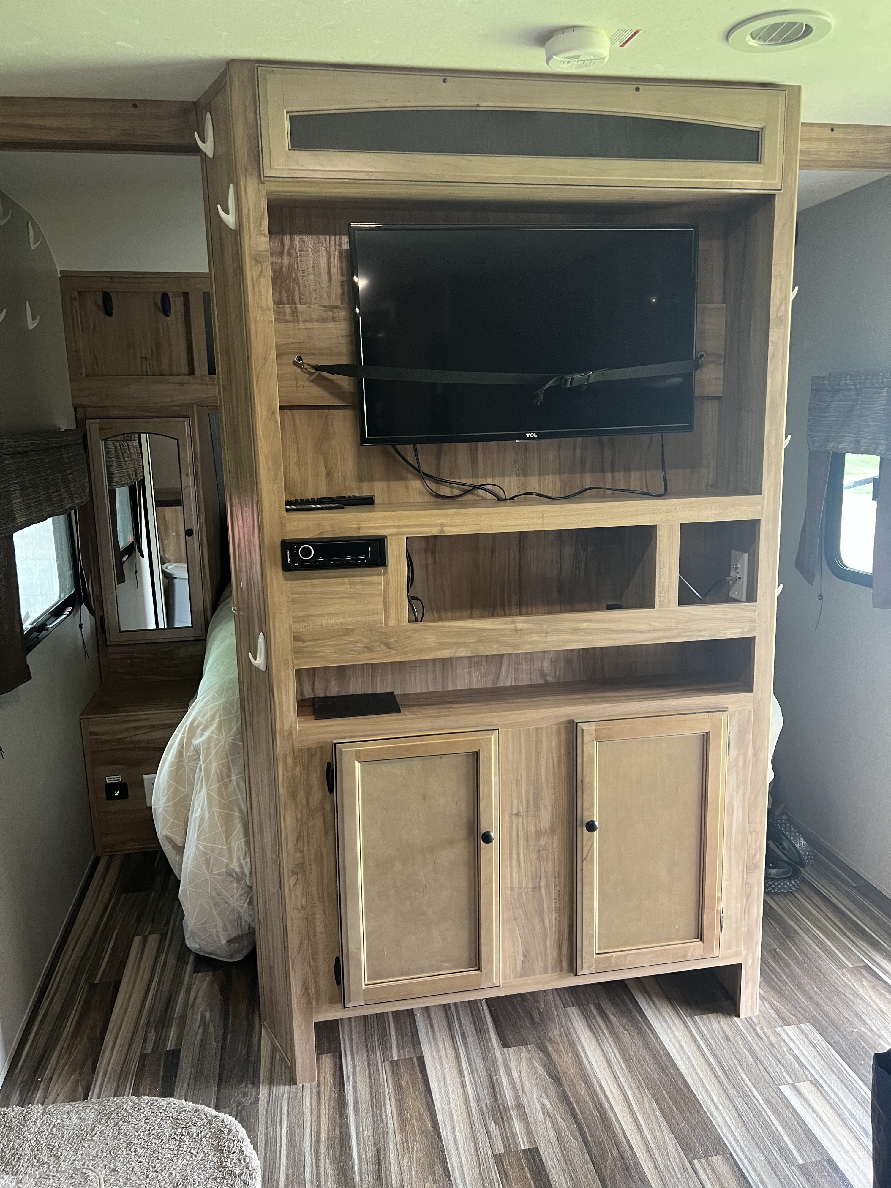 Inside an RV rental: a wooden entertainment unit with a strapped TV, shelves, cabinets, and a cozy bed with plank flooring.. Coachmen 29SE Bunkhouse 2019