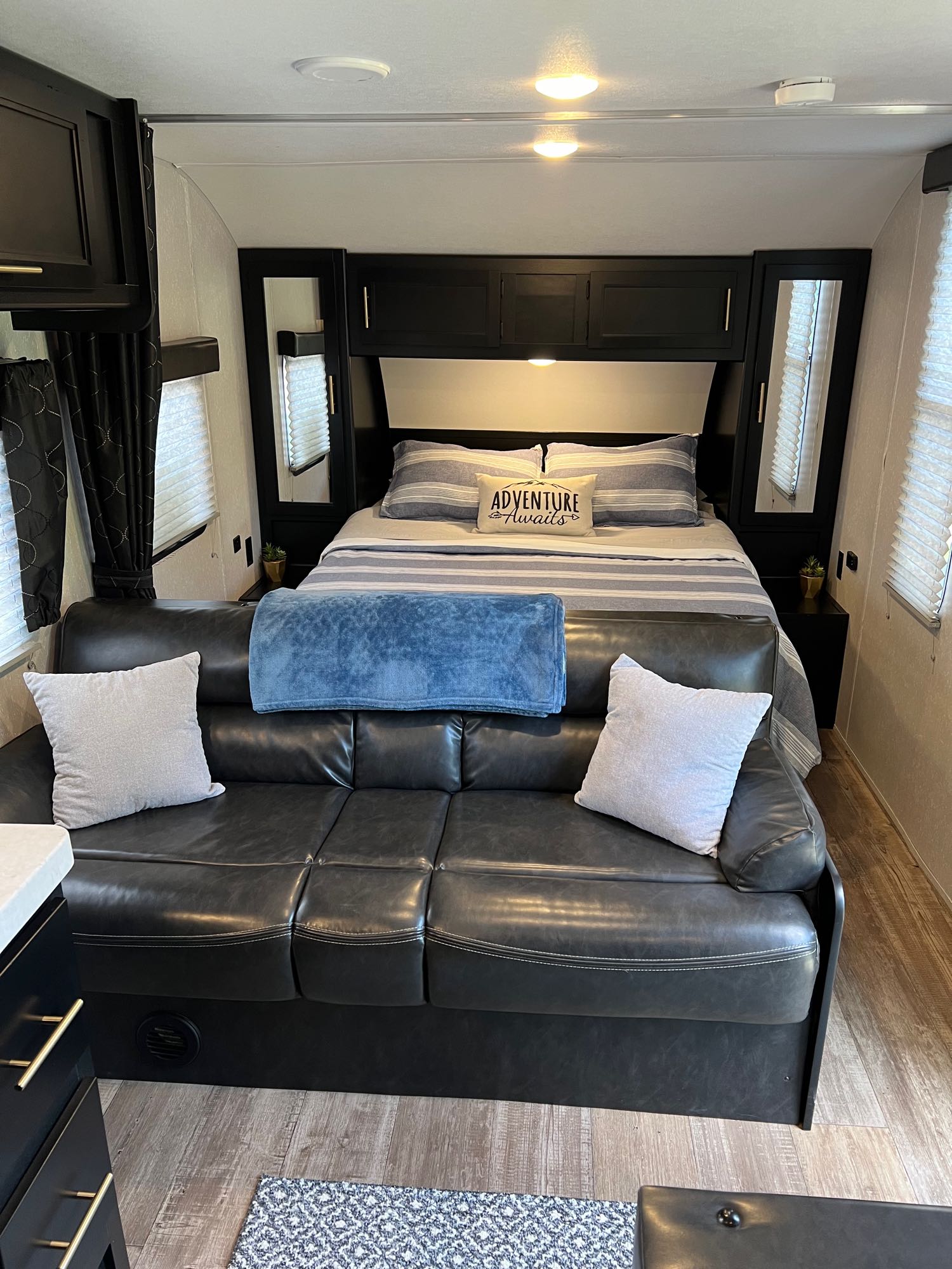 RV rental interior features a cozy bedroom with a striped bed and an adjacent living area with a dark leather sofa.. Forest River Cherokee Grey Wolf Limited 2021