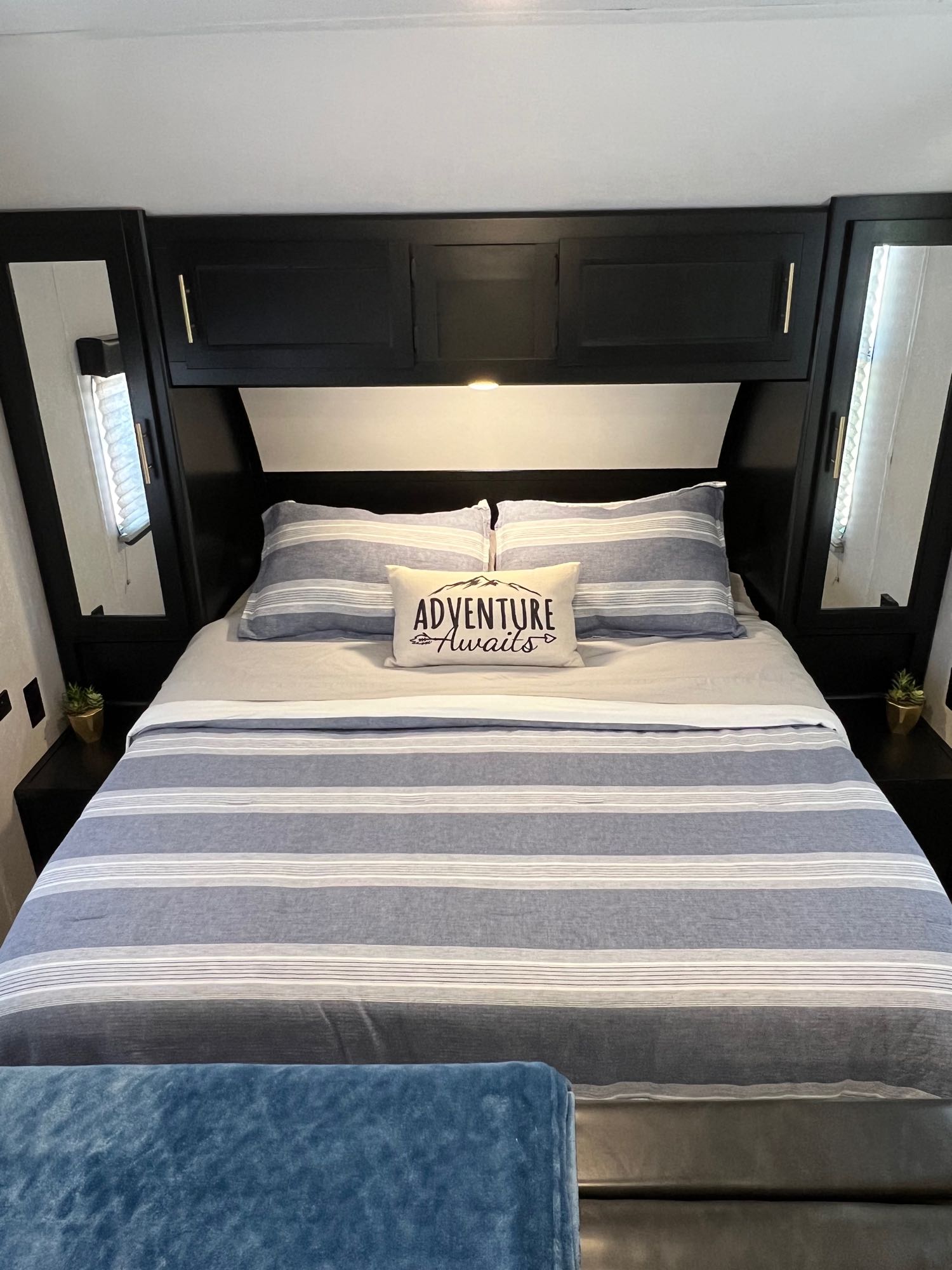 Cozy RV rental bedroom with striped bedding, "Adventure Awaits" pillow, and black built-in storage. Perfect for your next trip!. Forest River Cherokee Grey Wolf Limited 2021