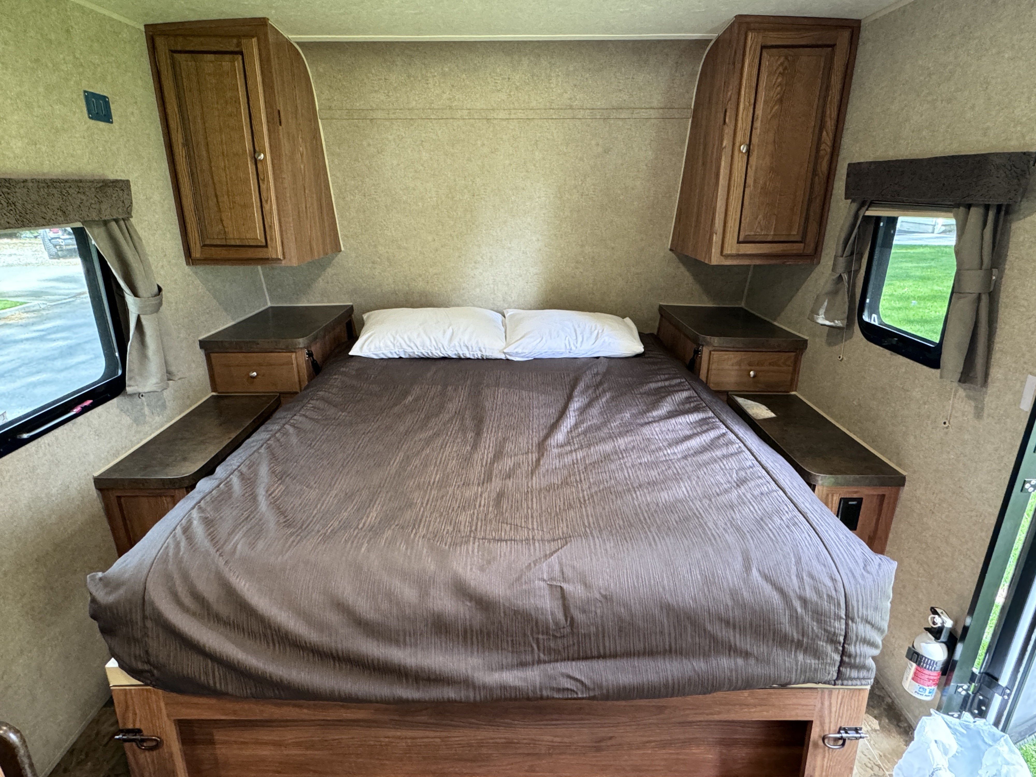 Cozy RV rental bedroom with bed, overhead cabinets, and bedside storage. Features side windows and TV mount for comfort.. Forest River Rockwood Mini Lite 2016