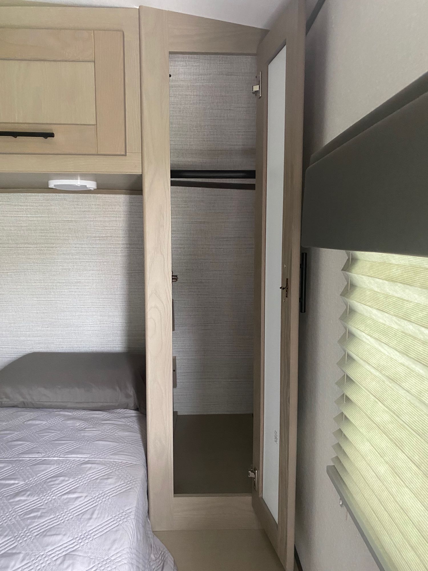 Inside an RV rental: a compact bedroom with a bed, light wood cabinet, open mirrored wardrobe, and pleated window blinds.. Cruiser RV Shadow Cruiser 2021