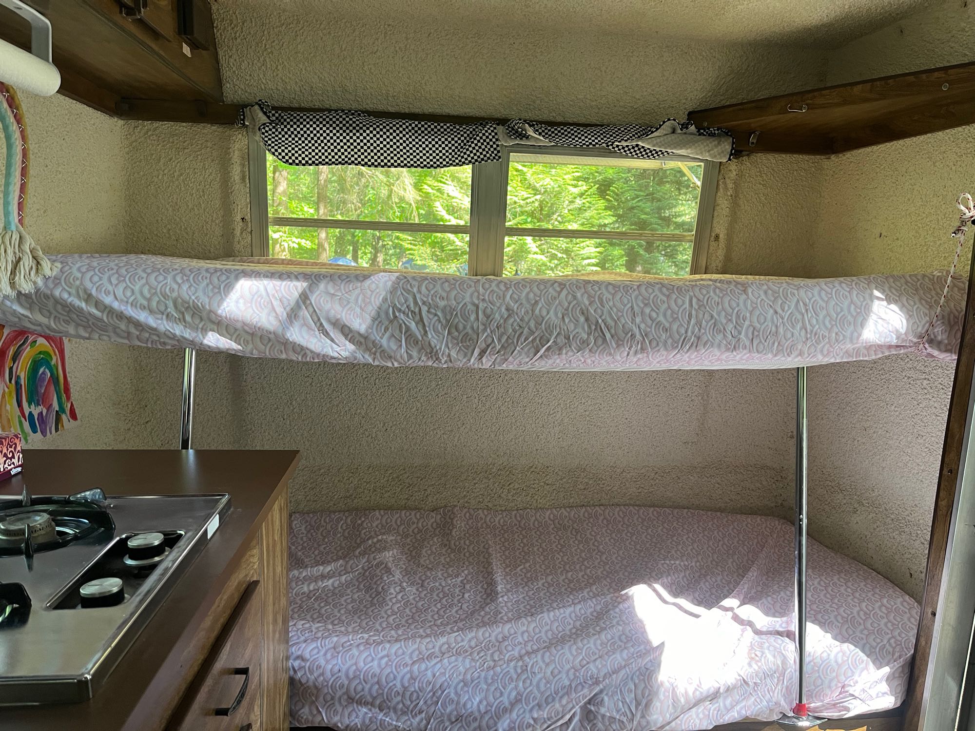 Cozy RV rental interior featuring bunk beds, a kitchenette, and a window view of green trees. Ideal for travel adventures.. Trillium Rv Jubilee 1980