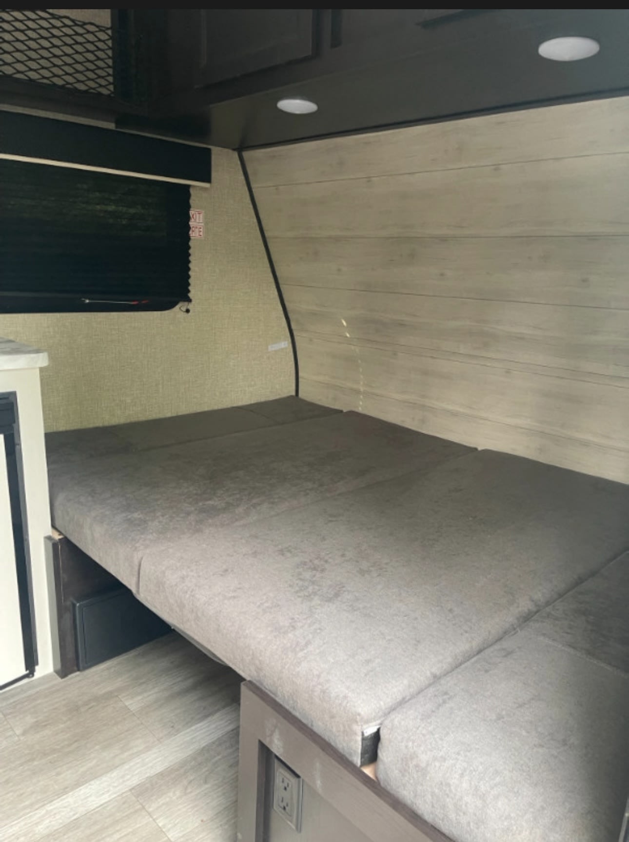 RV rental interior features a compact, comfy bed/seating area with wood paneling, a dark window shade, and overhead lights.. Jayco Jay Flight SLX 2022