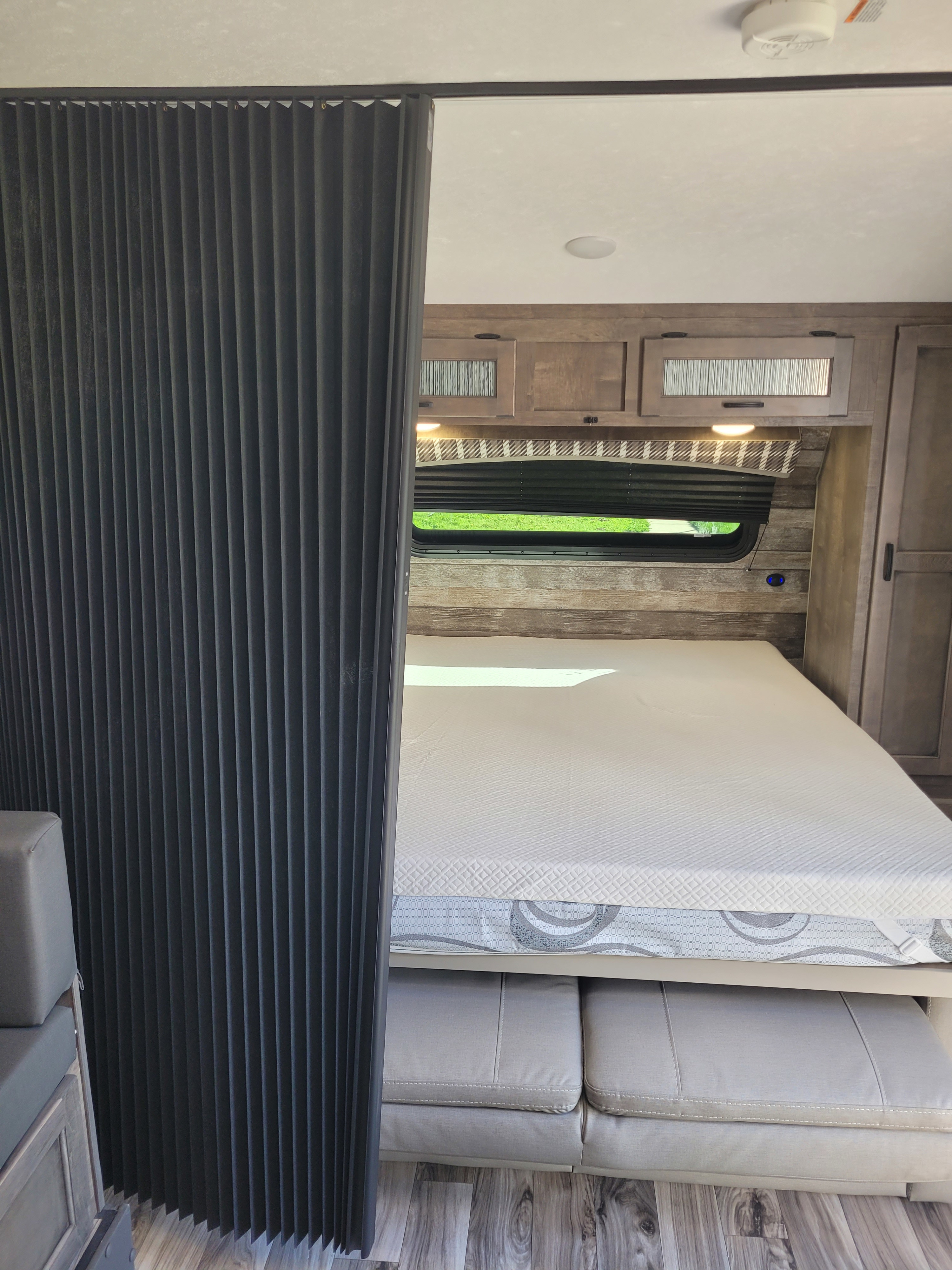 Inside a modern RV rental: a cozy bedroom with a large bed, accordion privacy curtain, and overhead cabinets.. Venture 220VBH 2022