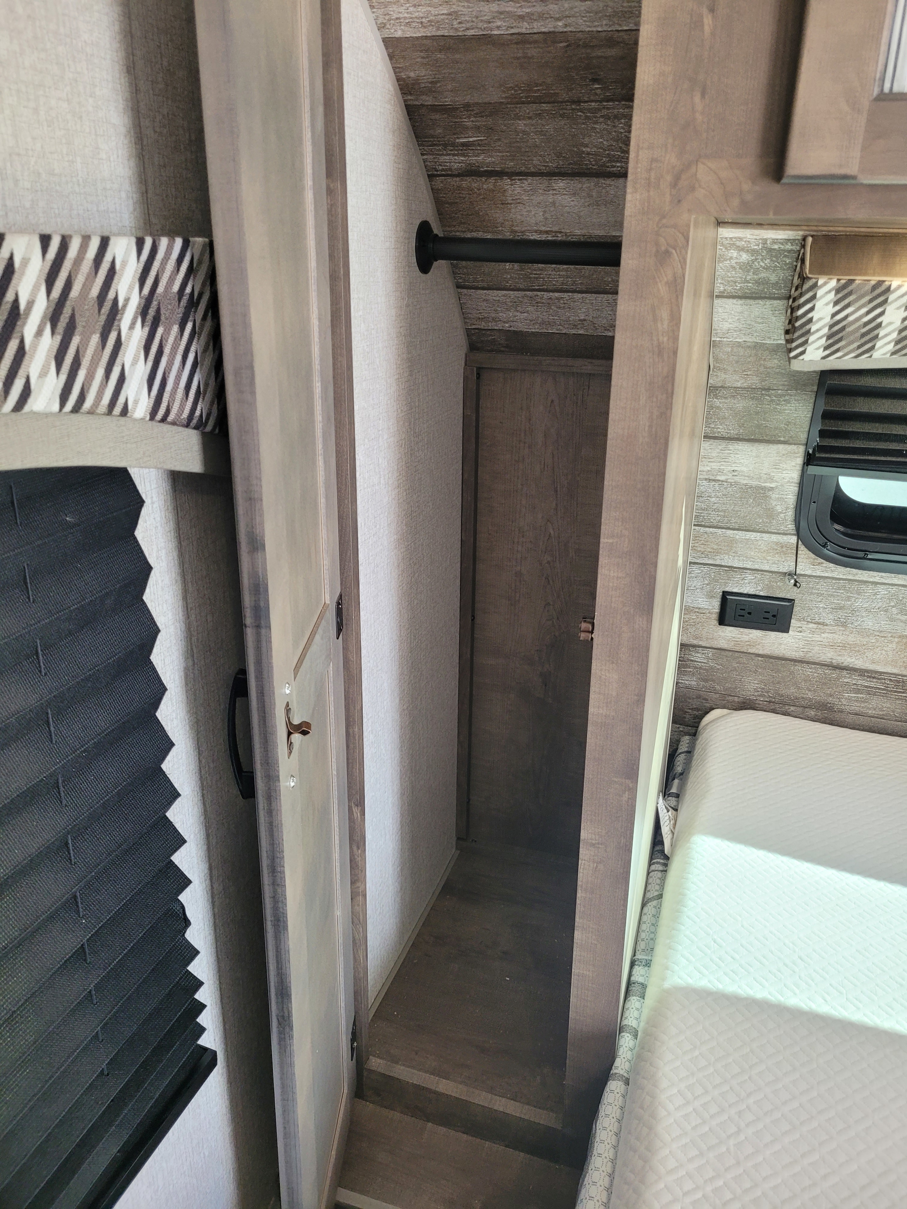 Inside an RV rental: a compact bedroom area with a bed, window, and small closet featuring a hanging rod.. Venture 220VBH 2022