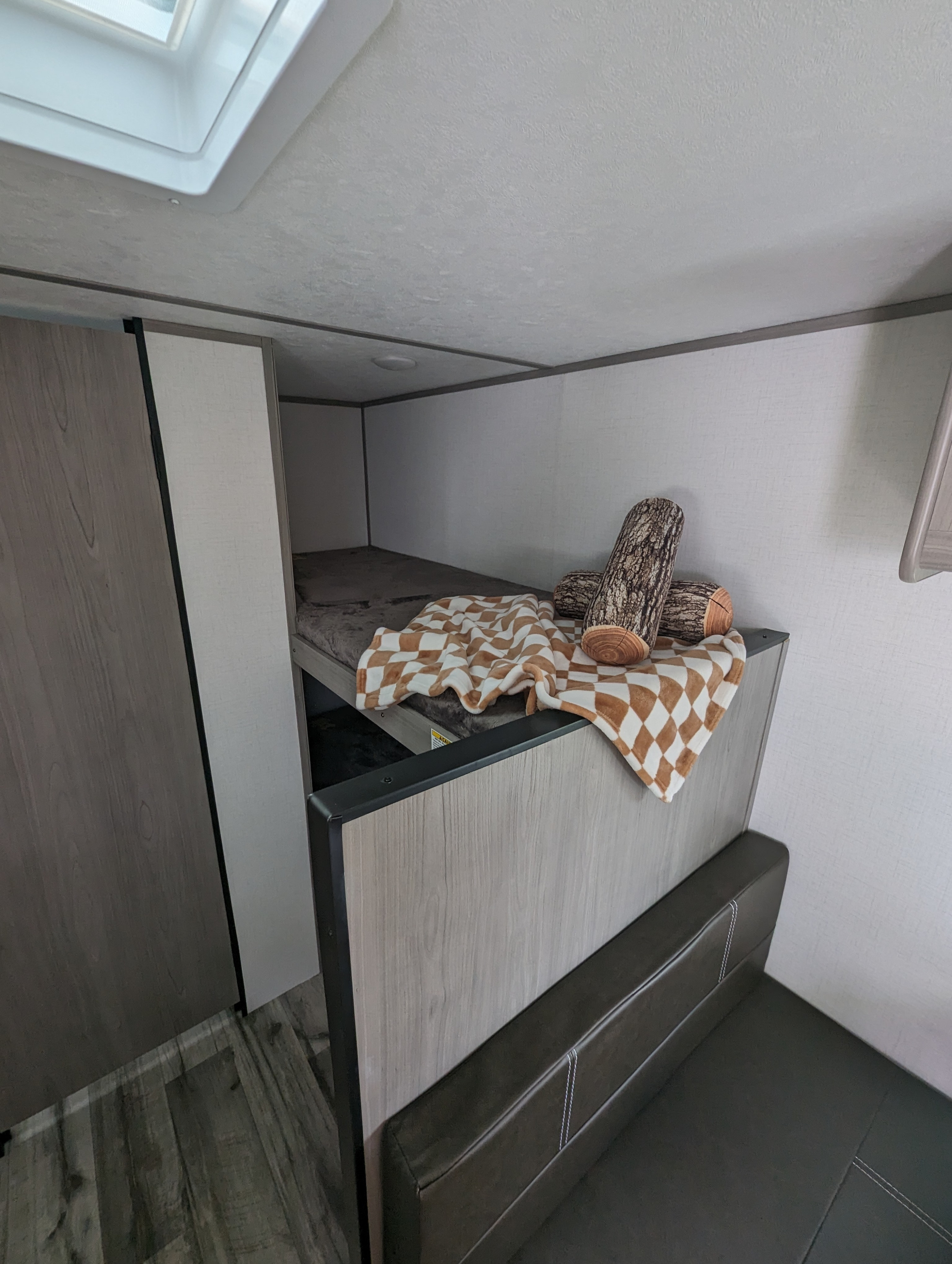 Cozy RV rental interior featuring a bunk bed with a checkered blanket and log pillows, plus a comfy seating area.. Dutchmen Coleman Lantern 17B 2024
