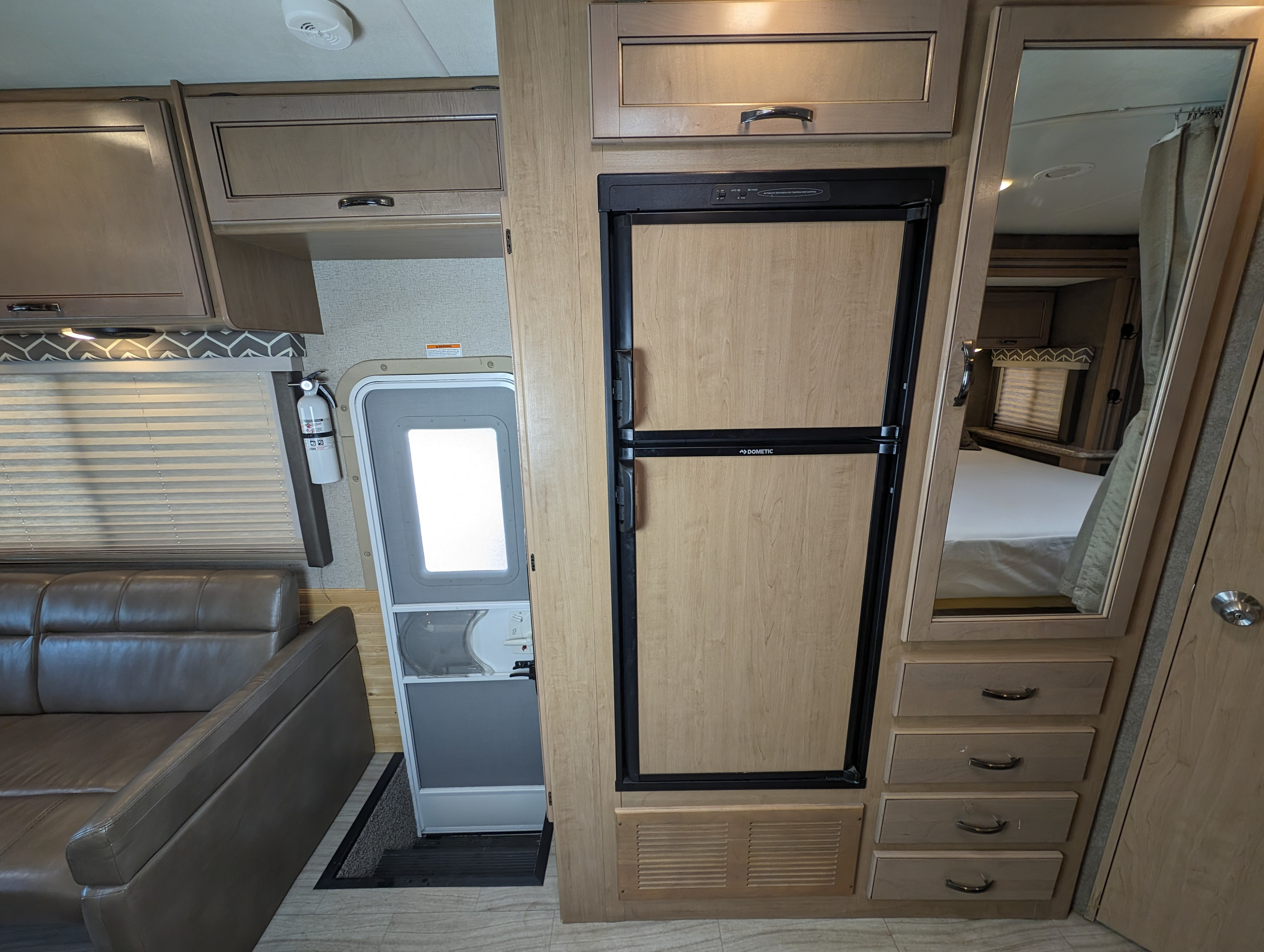 RV rental interior: cozy living space with a sofa, overhead cabinets, Dometic refrigerator, and a mirror reflecting the bedroom.. Thor Daybreak 2020