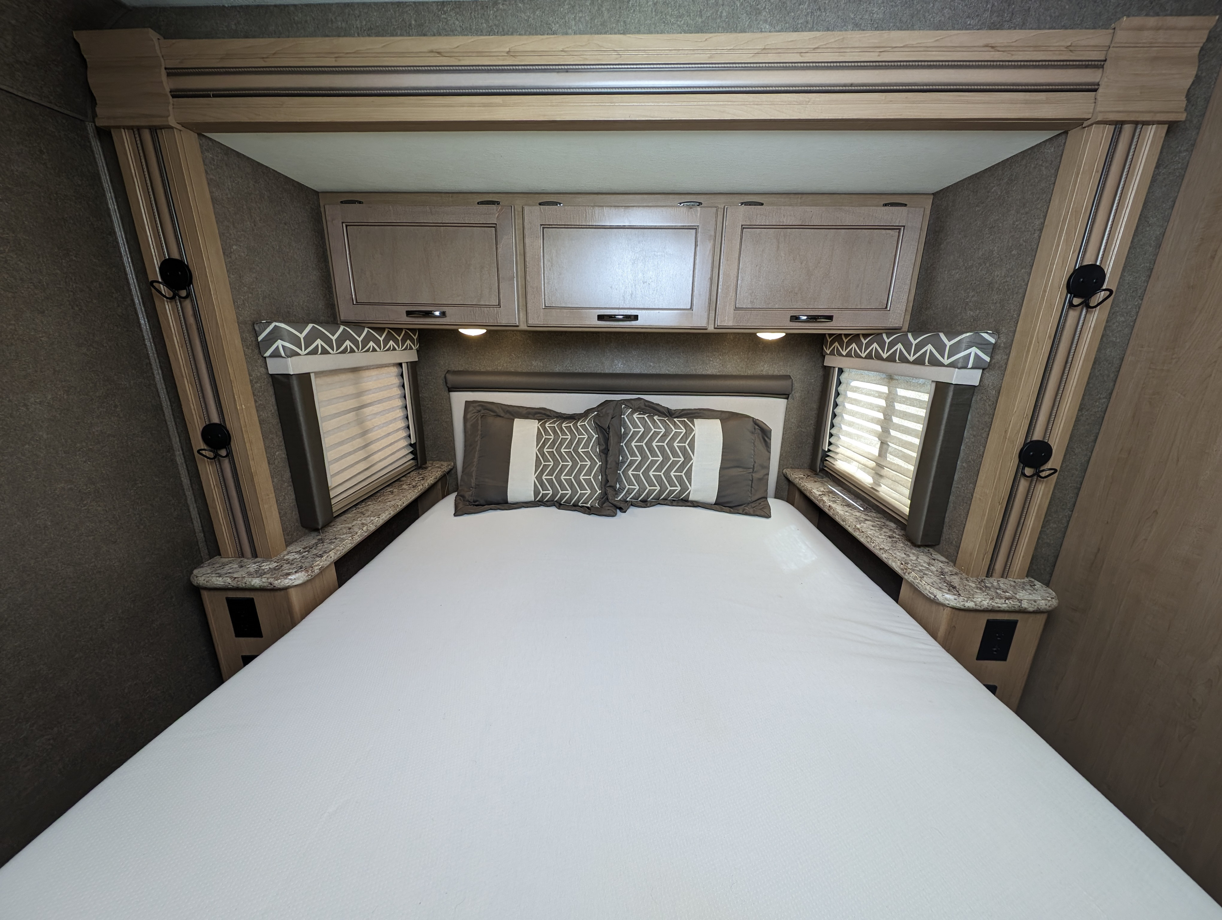 This comfortable RV rental bedroom features a clean bed, overhead cabinets, and windows with blinds, ideal for travel.. Thor Daybreak 2020