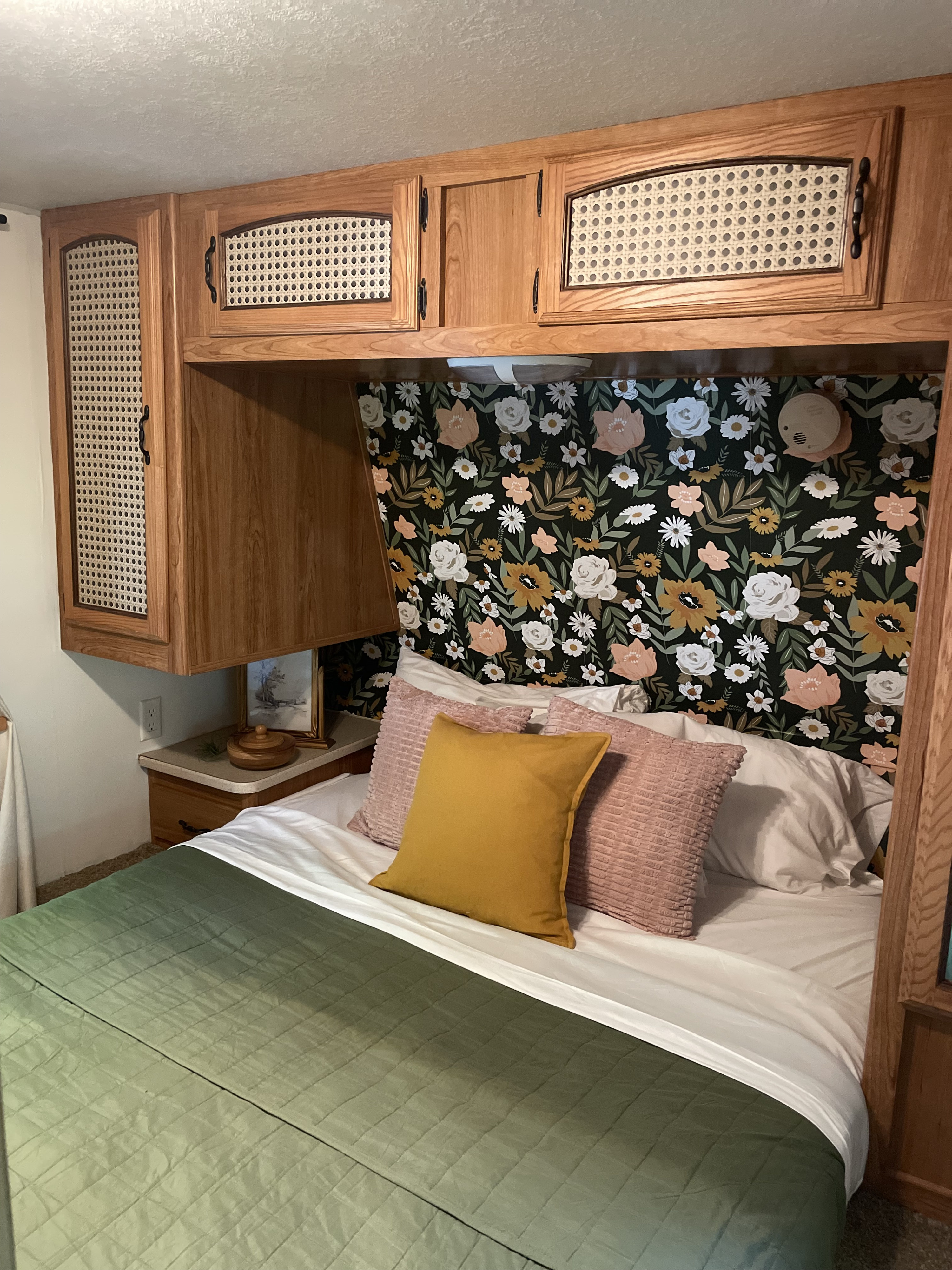 An inviting RV rental bedroom with custom floral wallpaper, cane cabinets, and a comfy bed setup.. Forest River Palomino Puma 2010