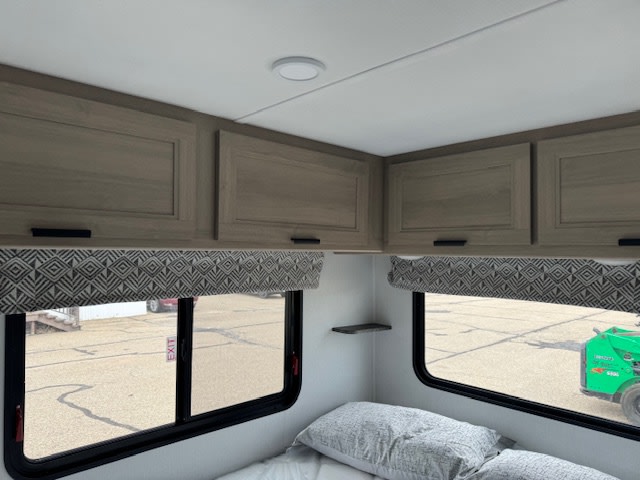 Comfortable RV rental bedroom featuring light wood cabinets, patterned valances, and large windows with views. Perfect for travel!. Forest River 2351LE 2024