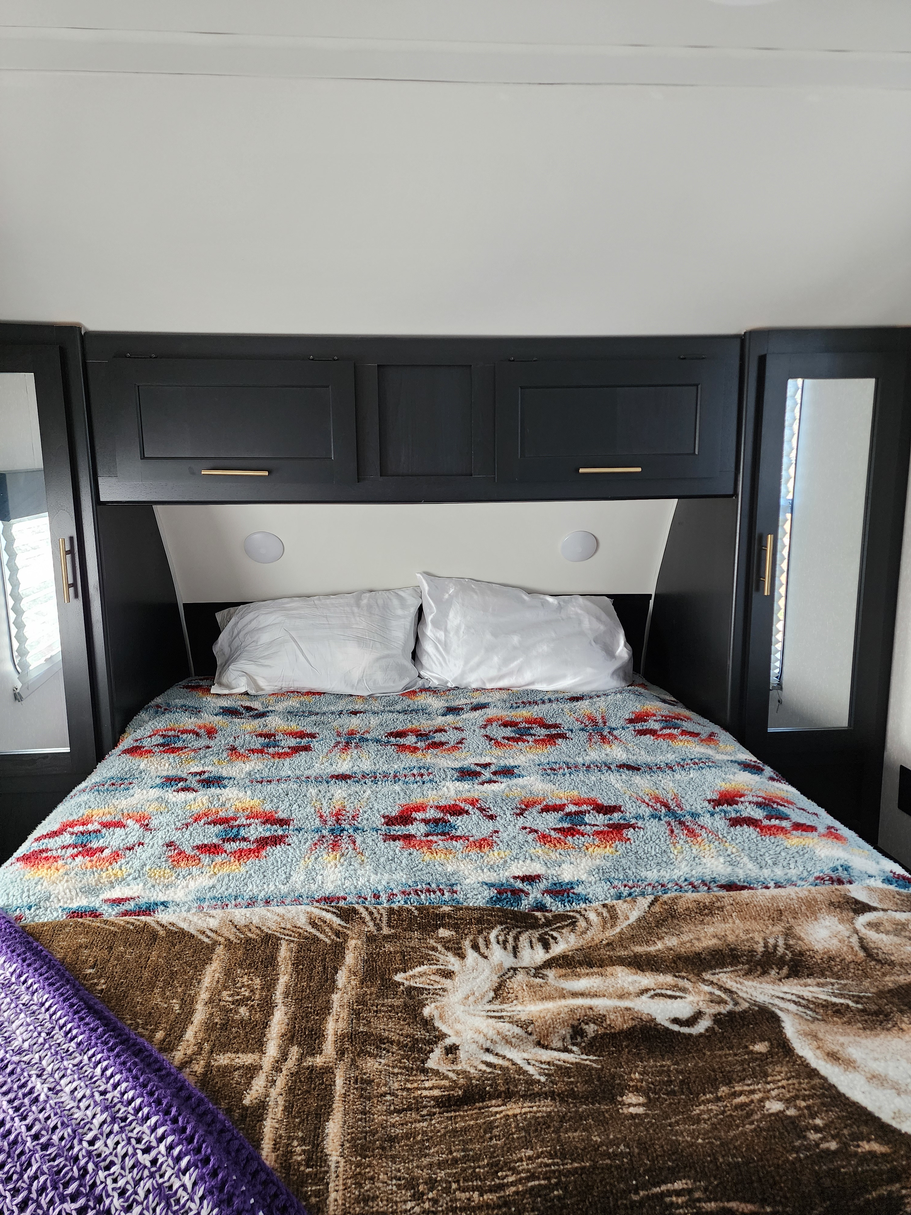 Cozy RV rental bedroom: bed with white pillows, colorful blankets, dark overhead storage, and bedside lights. Ready for travel!. Forest River Cherokee Grey Wolf 2022