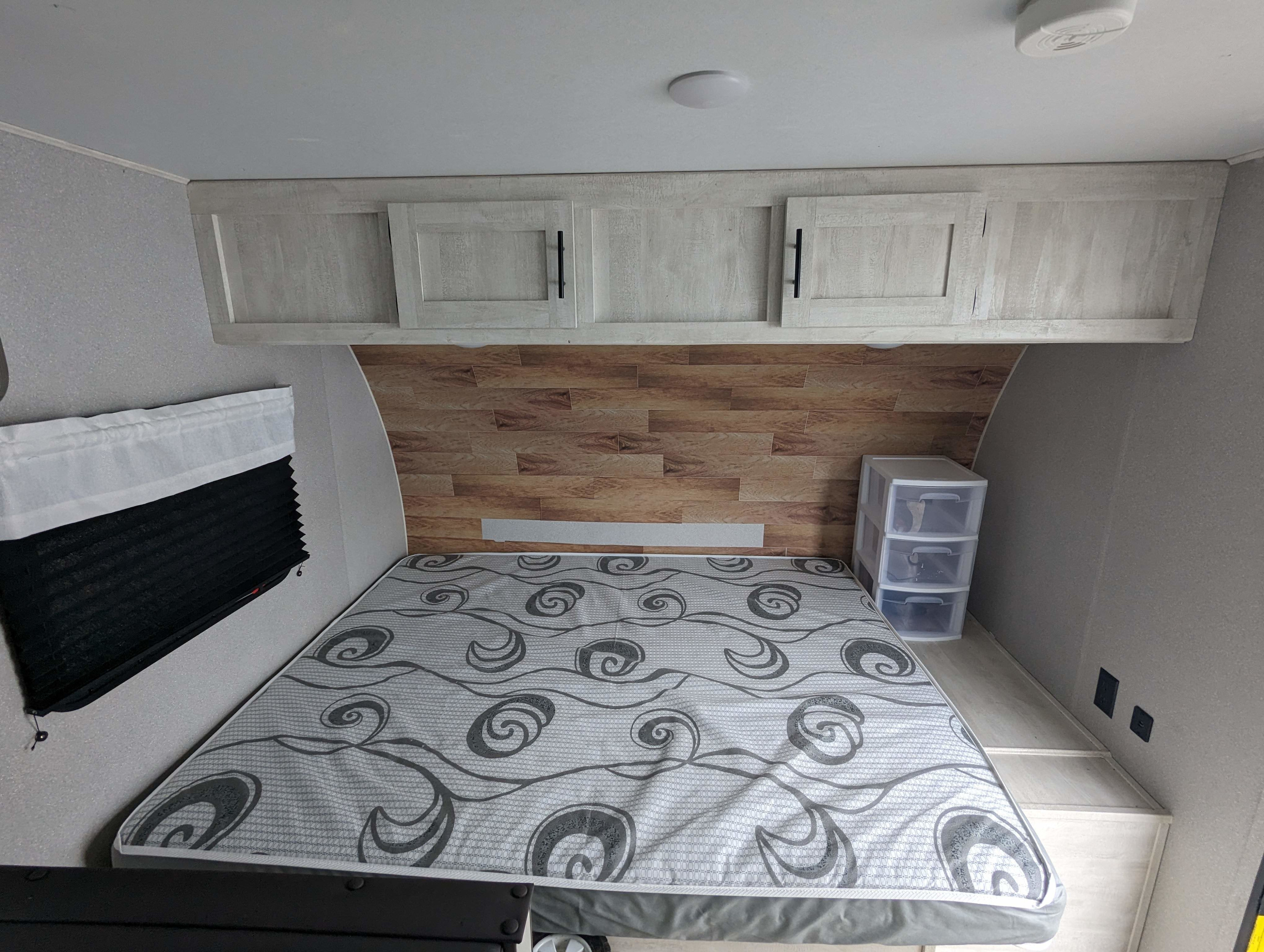 RV rental bedroom: a comfy mattress with grey swirls, light wood cabinets, wood accent wall, and plastic storage unit.. Grand River Comfortline 20bh 2022