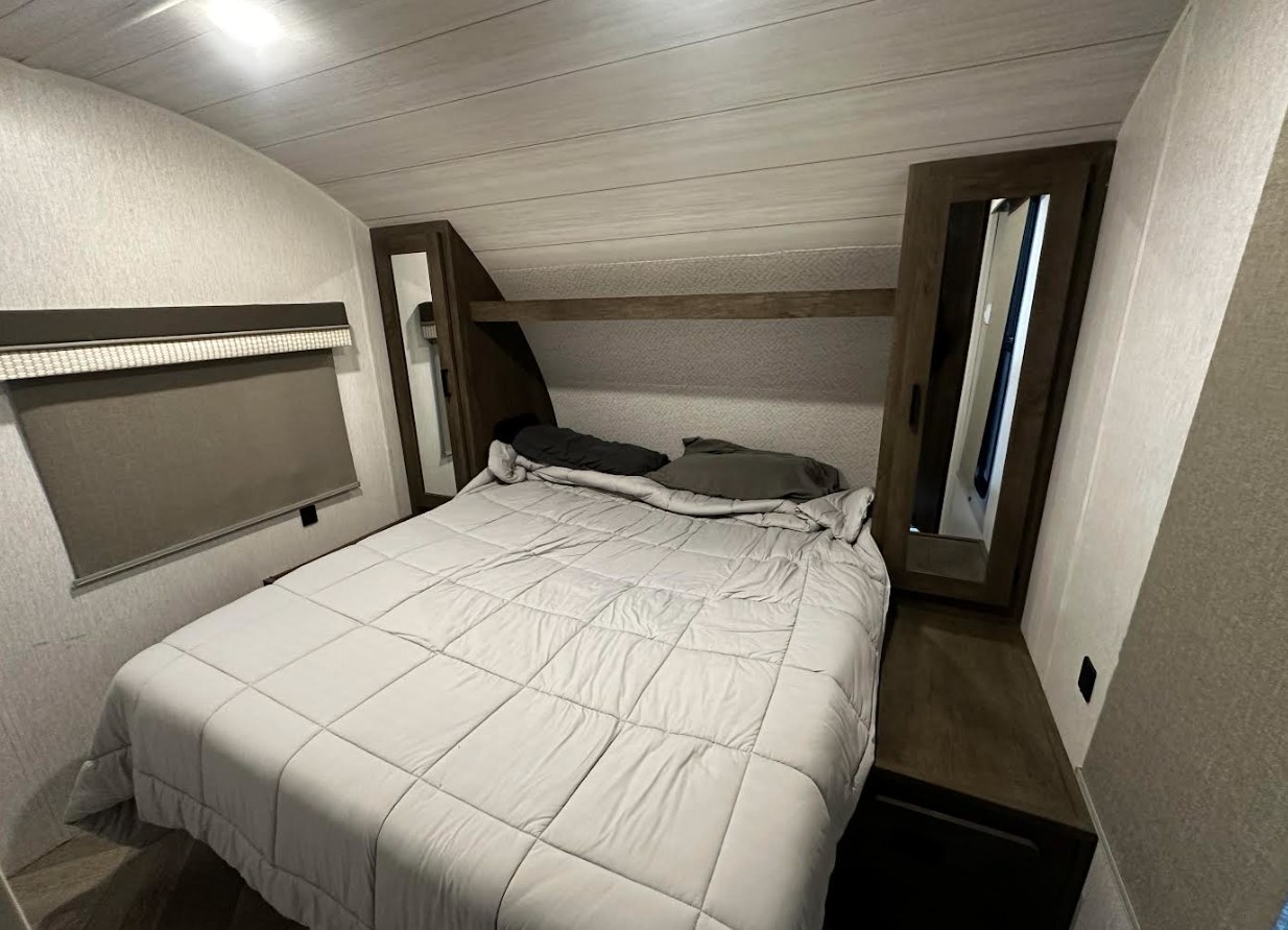 Inside an RV rental: a cozy bedroom with a bed, window with shade, and mirrored storage cabinets.. Forest River Salem Cruise Lite 2023