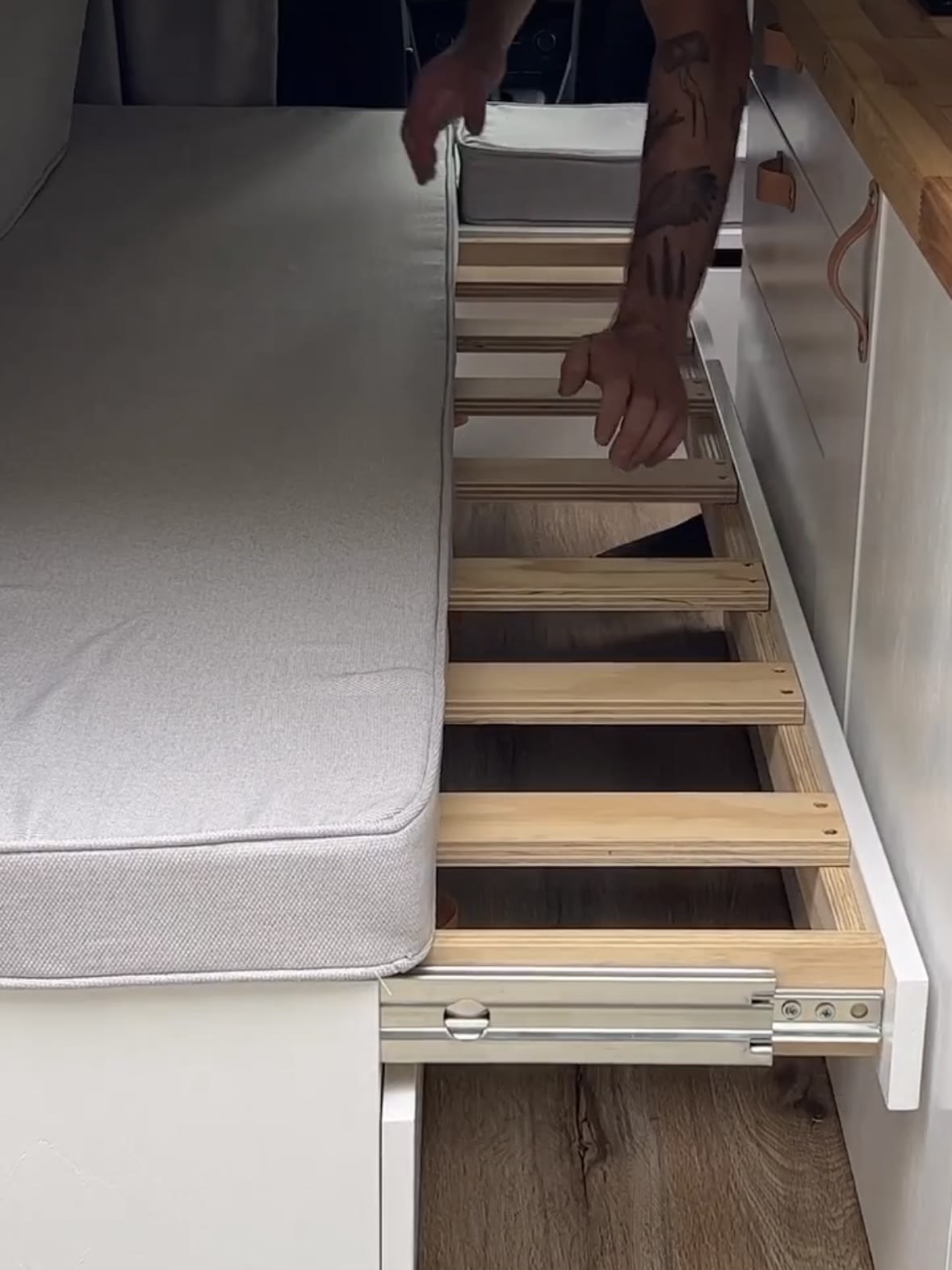 Expanding an RV rental's pull-out bed: A person extends the slatted frame from under the gray cushion.. Ford Transit Custom 2019