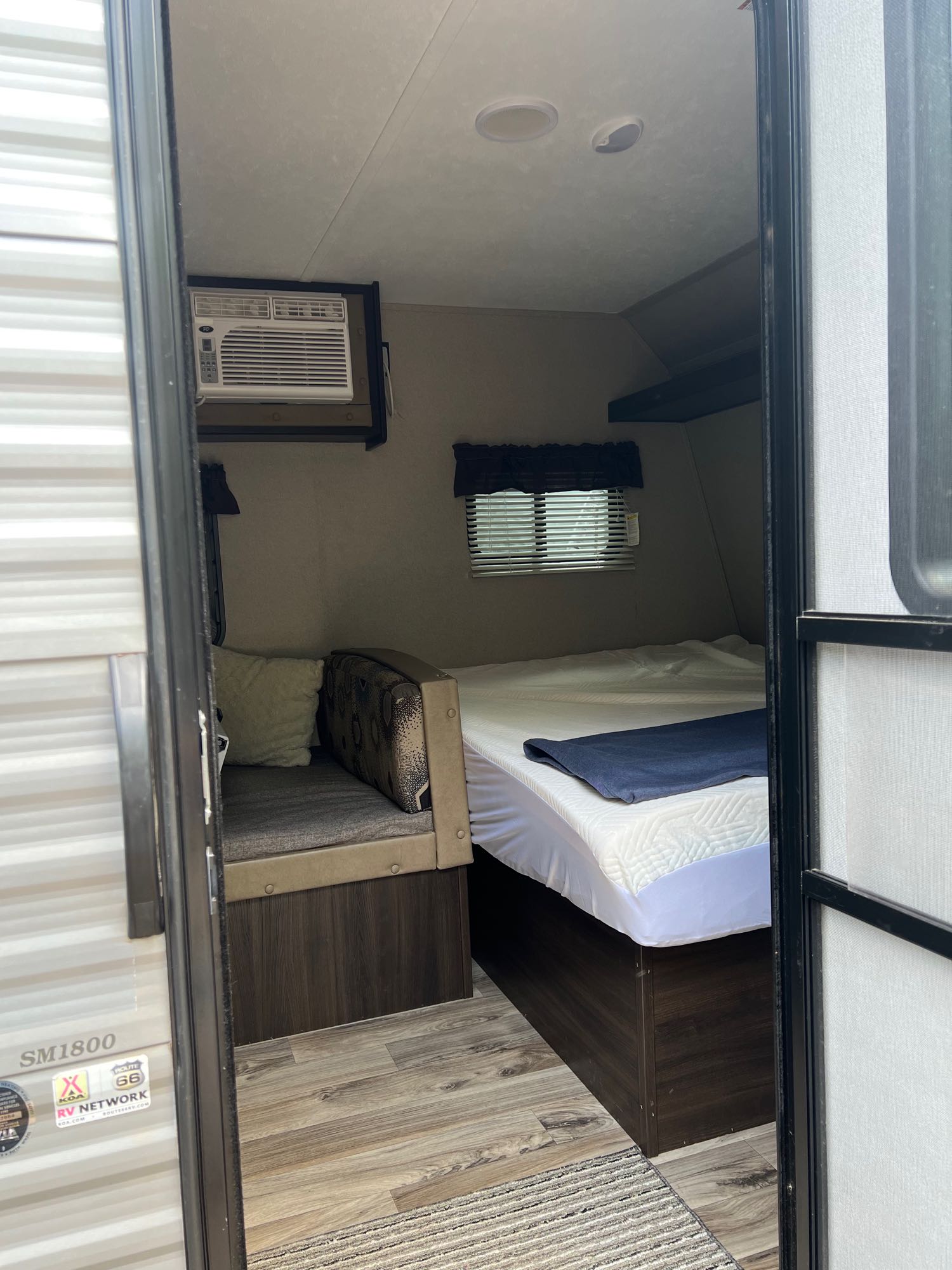 Interior of an RV rental showing a cozy bed, a small couch, and an air conditioner, ideal for travel.. Keystone RV Springdale 2018
