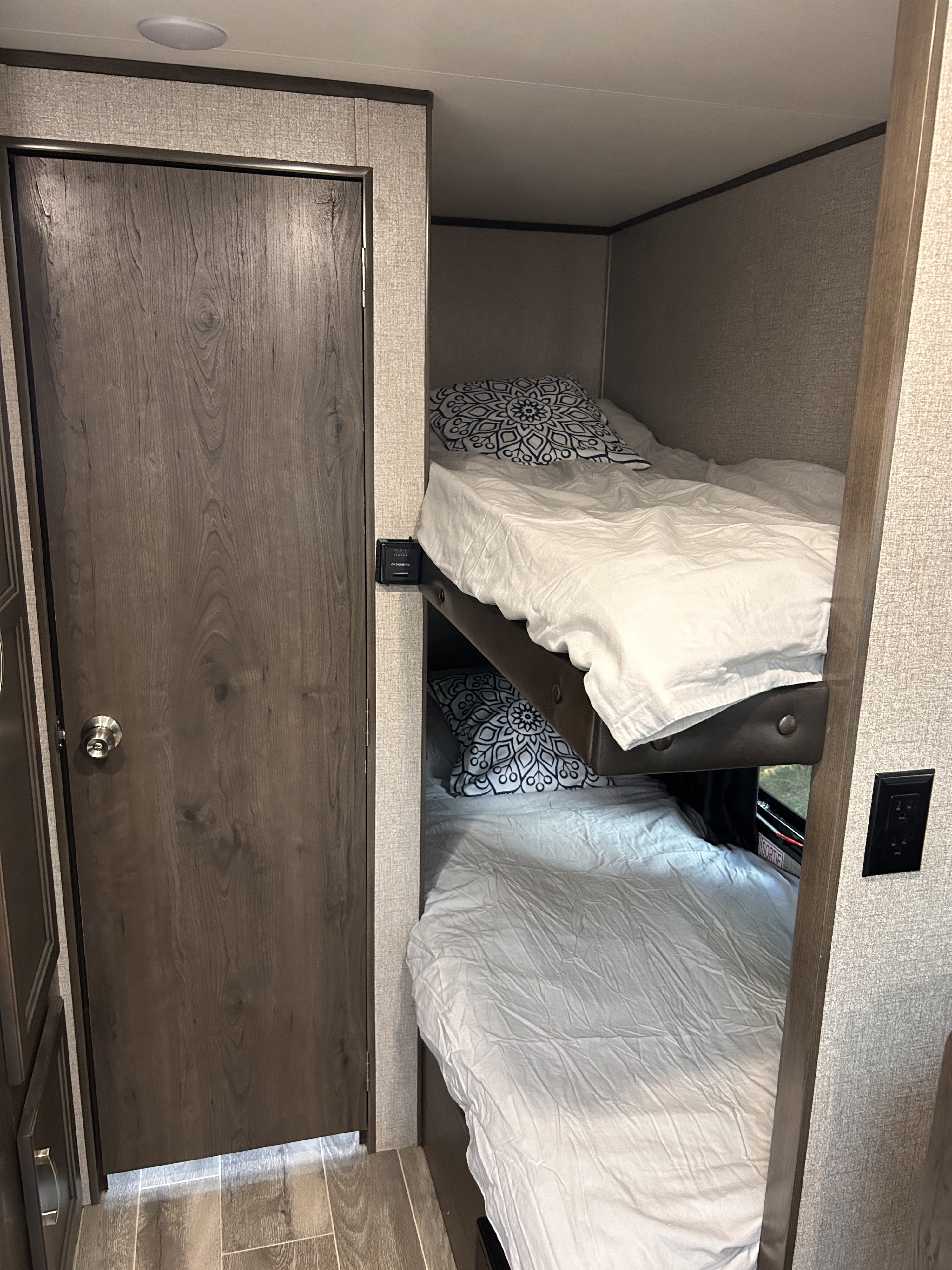 Inside an RV rental, discover these functional bunk beds with white sheets, patterned pillows, and accessible controls and outlets.. Jayco Jay Flight SLX 2021