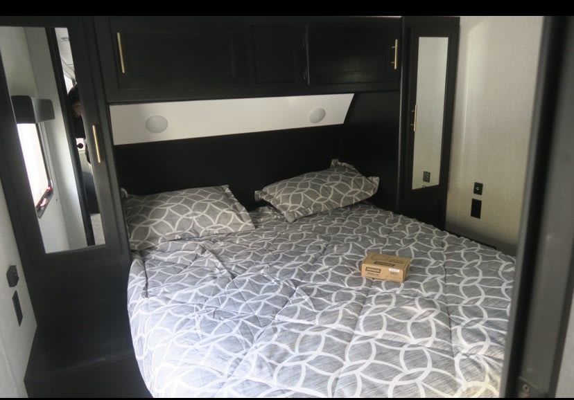 This RV rental offers a cozy bedroom with a patterned bed, overhead storage, and mirrored wardrobes.. Forest River Cherokee Grey Wolf Black Label 2023