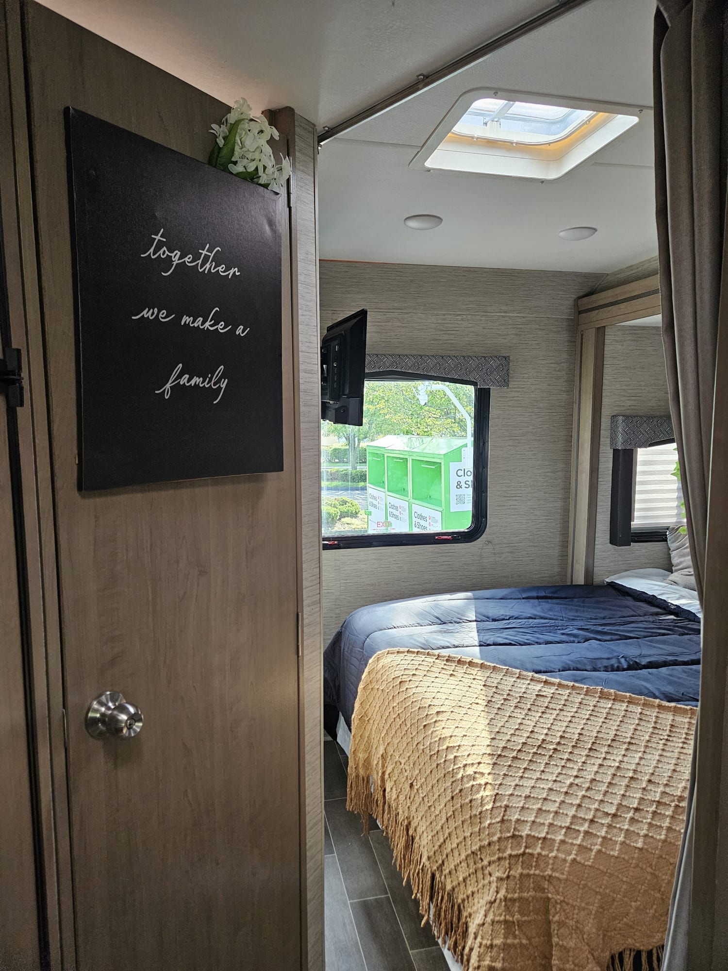Cozy RV rental bedroom showing a bed, decorative sign, and window view of a green donation bin.. Thor Chateau 2022
