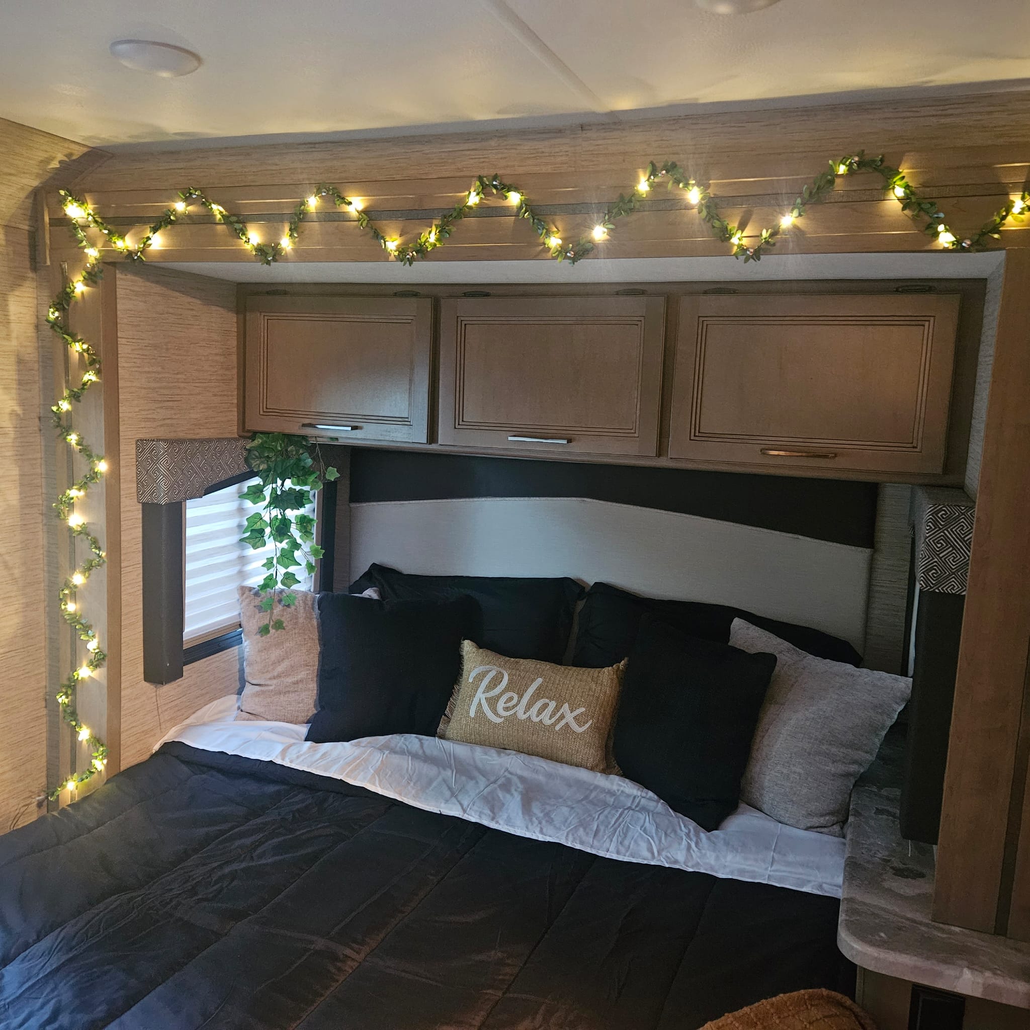 Cozy RV rental bedroom with glowing leaf string lights, a "Relax" pillow, and overhead cabinets for a comfortable stay.. Thor Chateau 2022