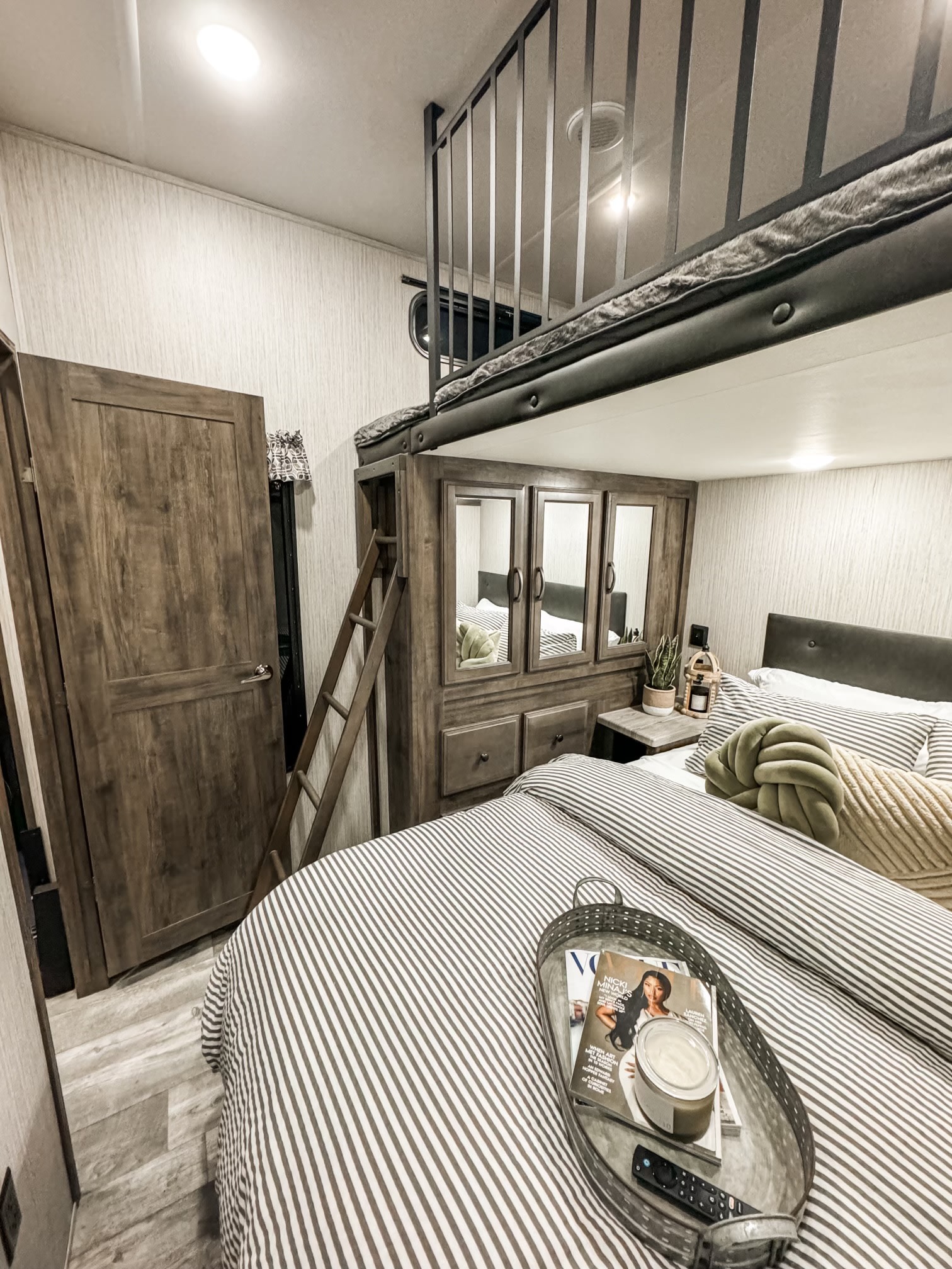 Relaxing RV rental bedroom showing a striped main bed, overhead loft bunk, and built-in storage.. Forest River Sierra 2022