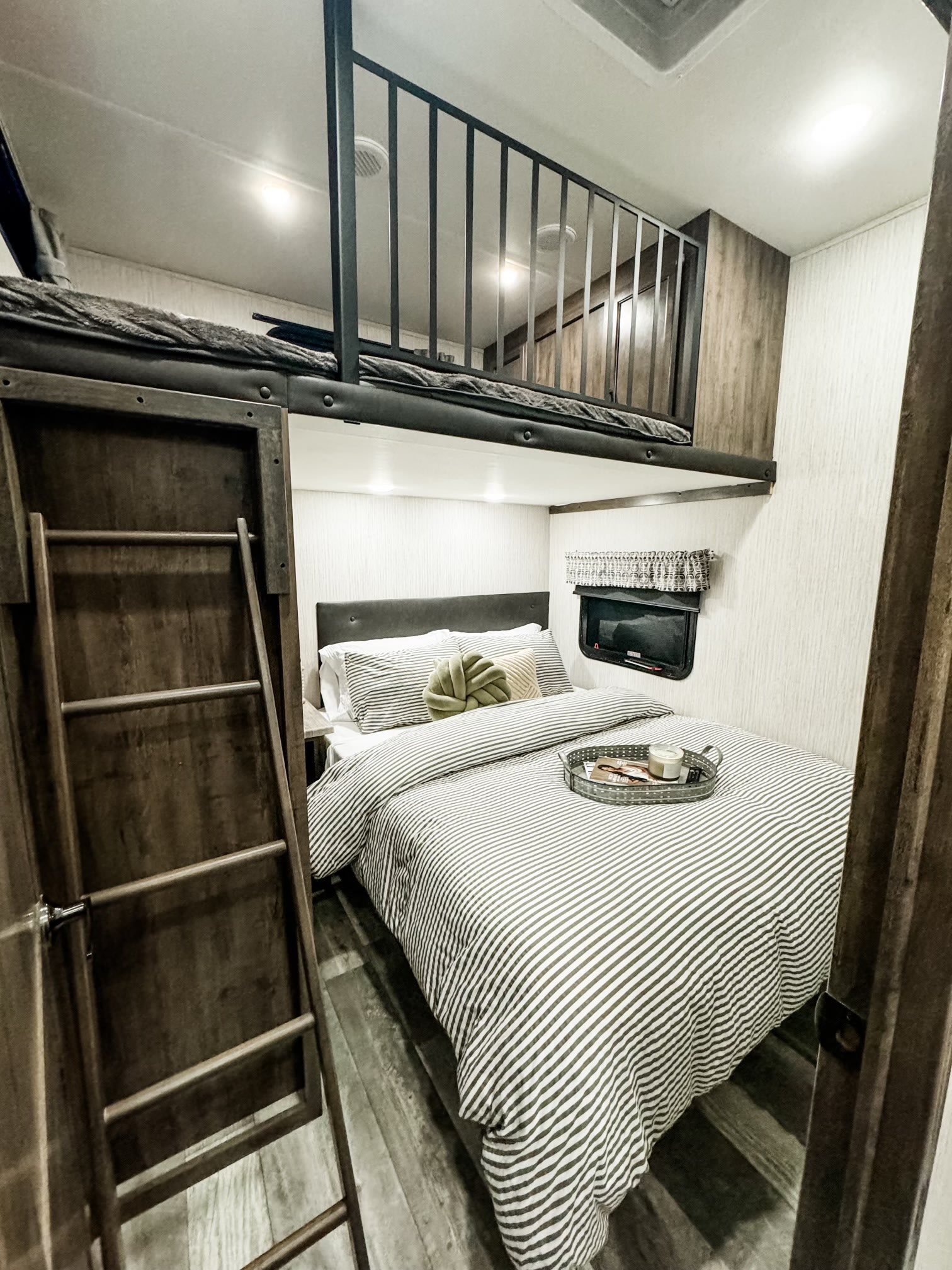 Cozy RV rental bedroom featuring a striped main bed, upper bunk with railing, and a ladder for access.. Forest River Sierra 2022